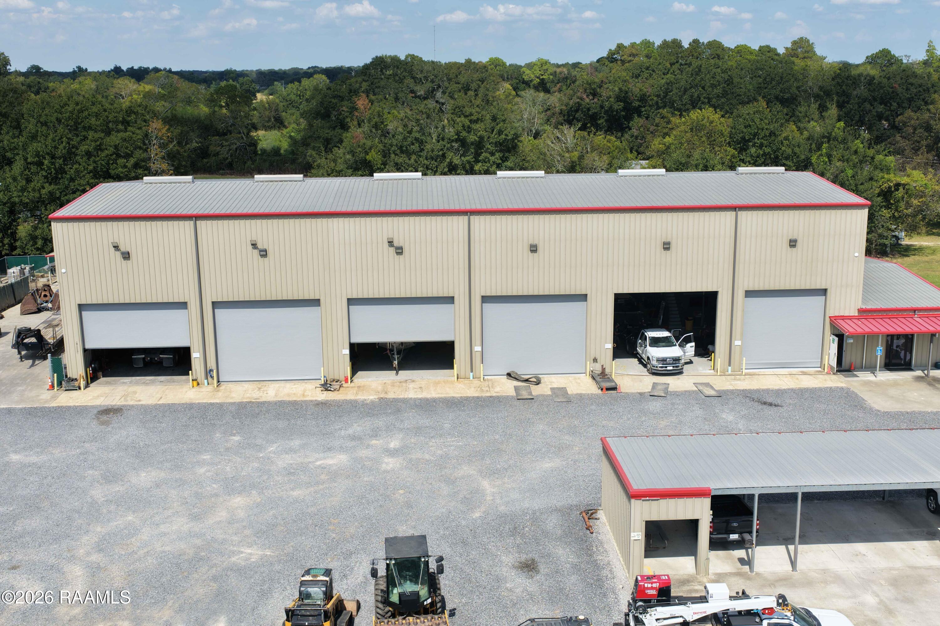Commercial workshop with multiple roll-up garage doors and a gravel yard, viewed from above.