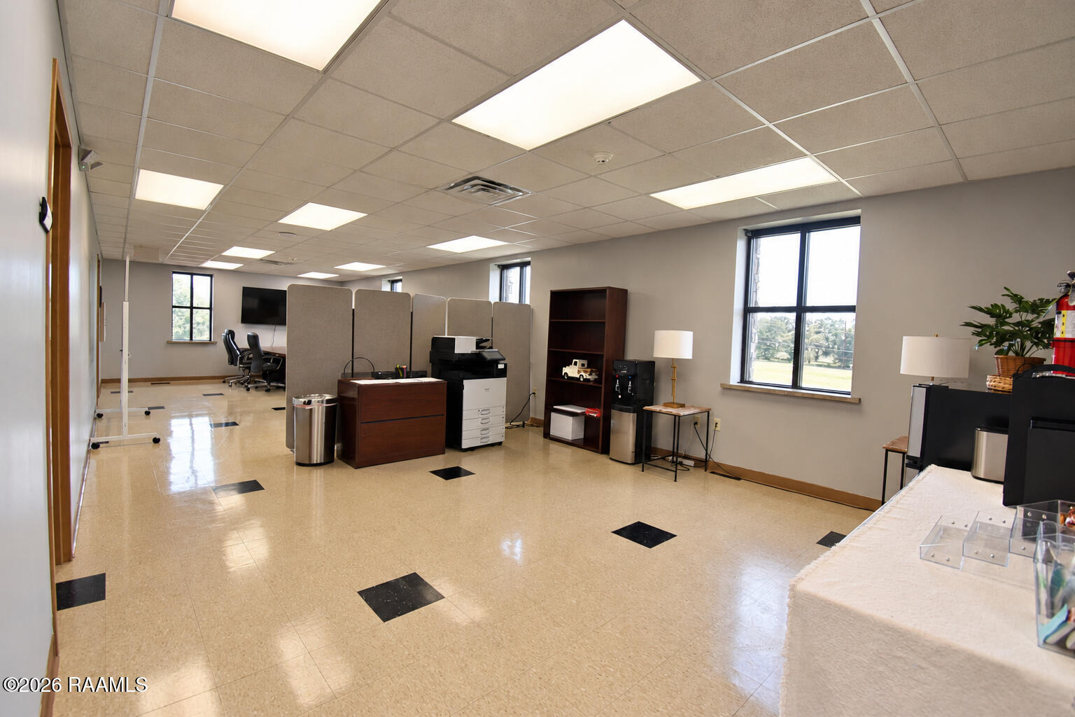 Furnished office with work partitions, copier, shelving, and large windows overlooking a lawn.