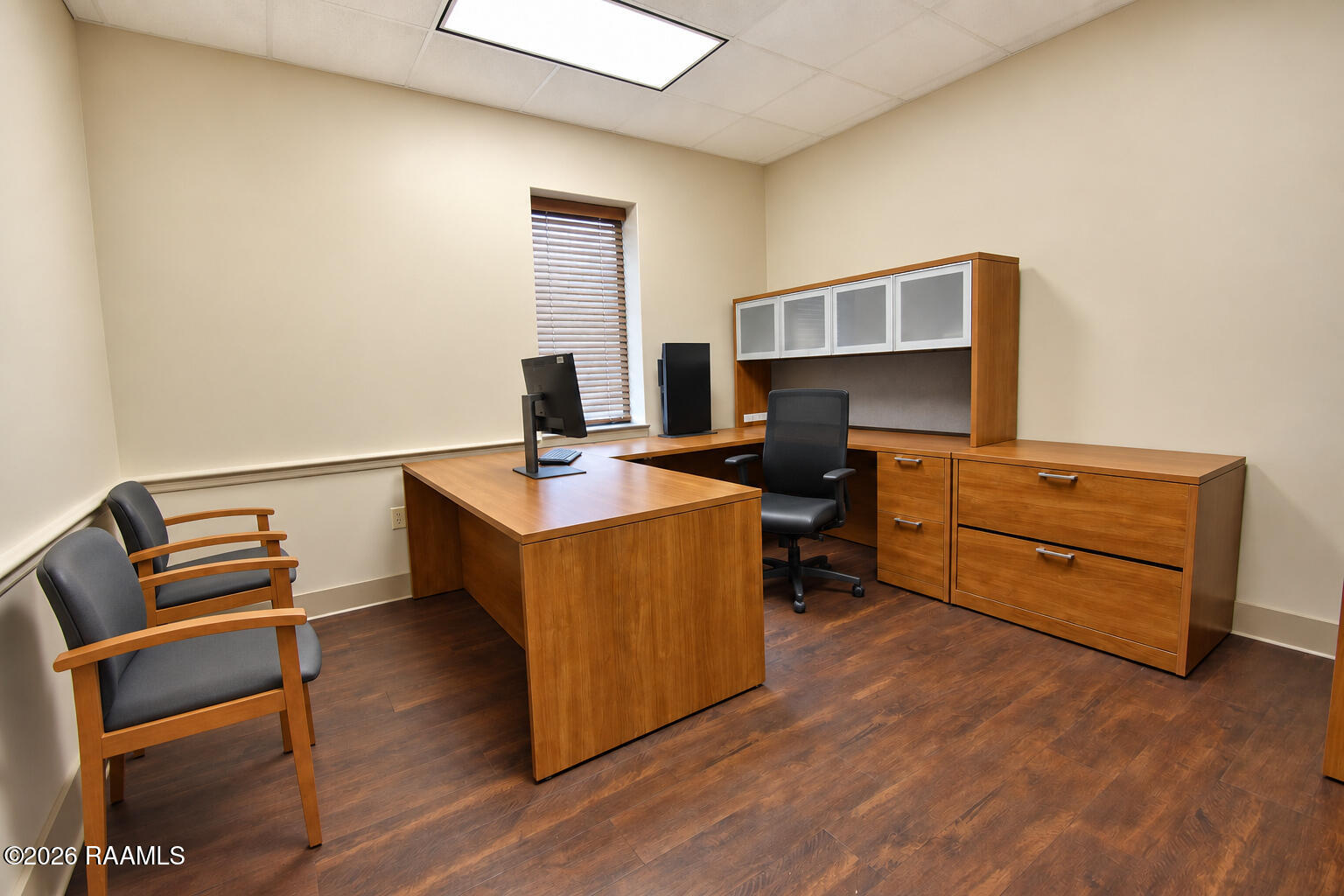 Office with a large wooden desk, matching cabinetry, and two guest chairs.