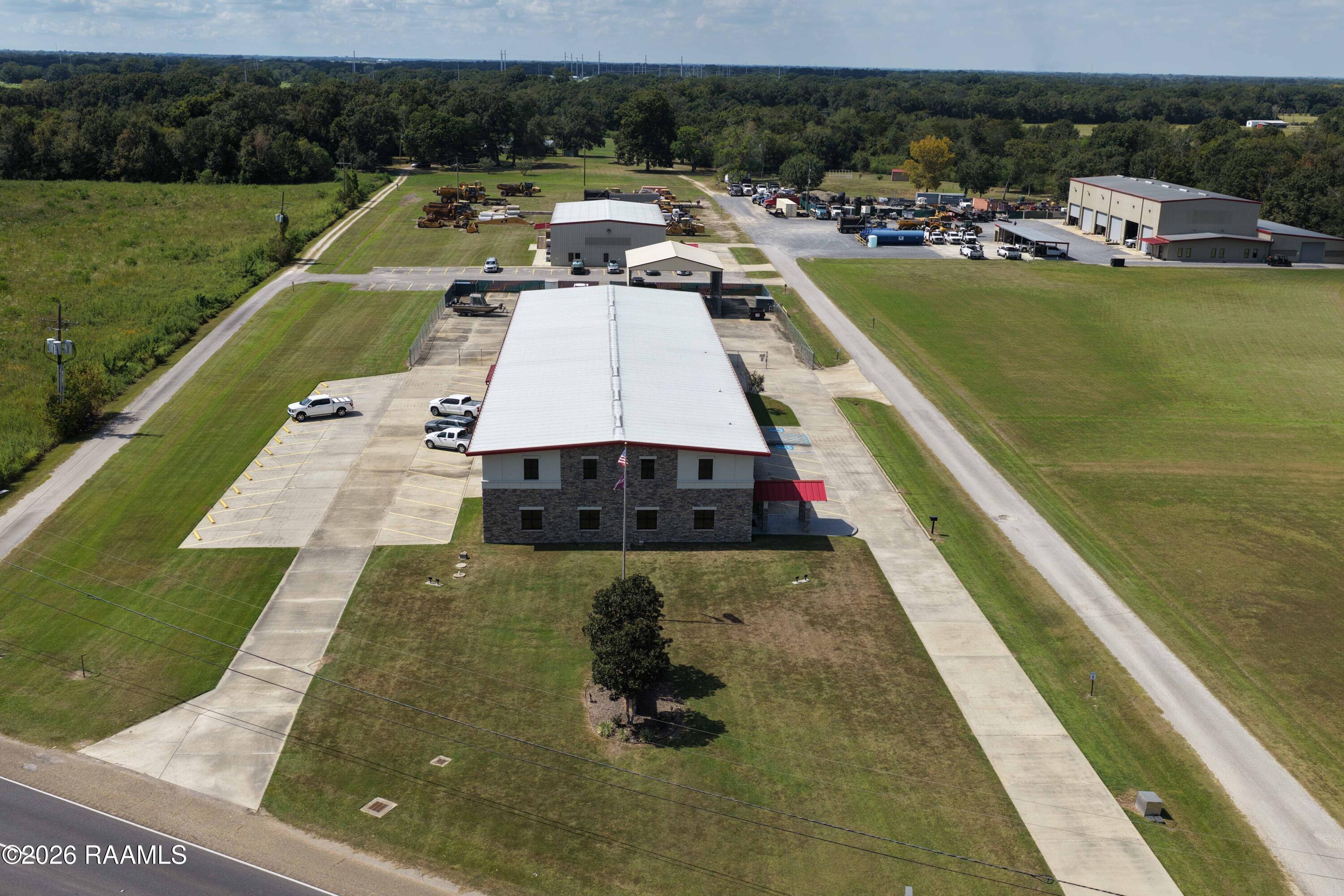 Aerial view of a two-story commercial building with a white roof, parking areas, and expansive grounds.