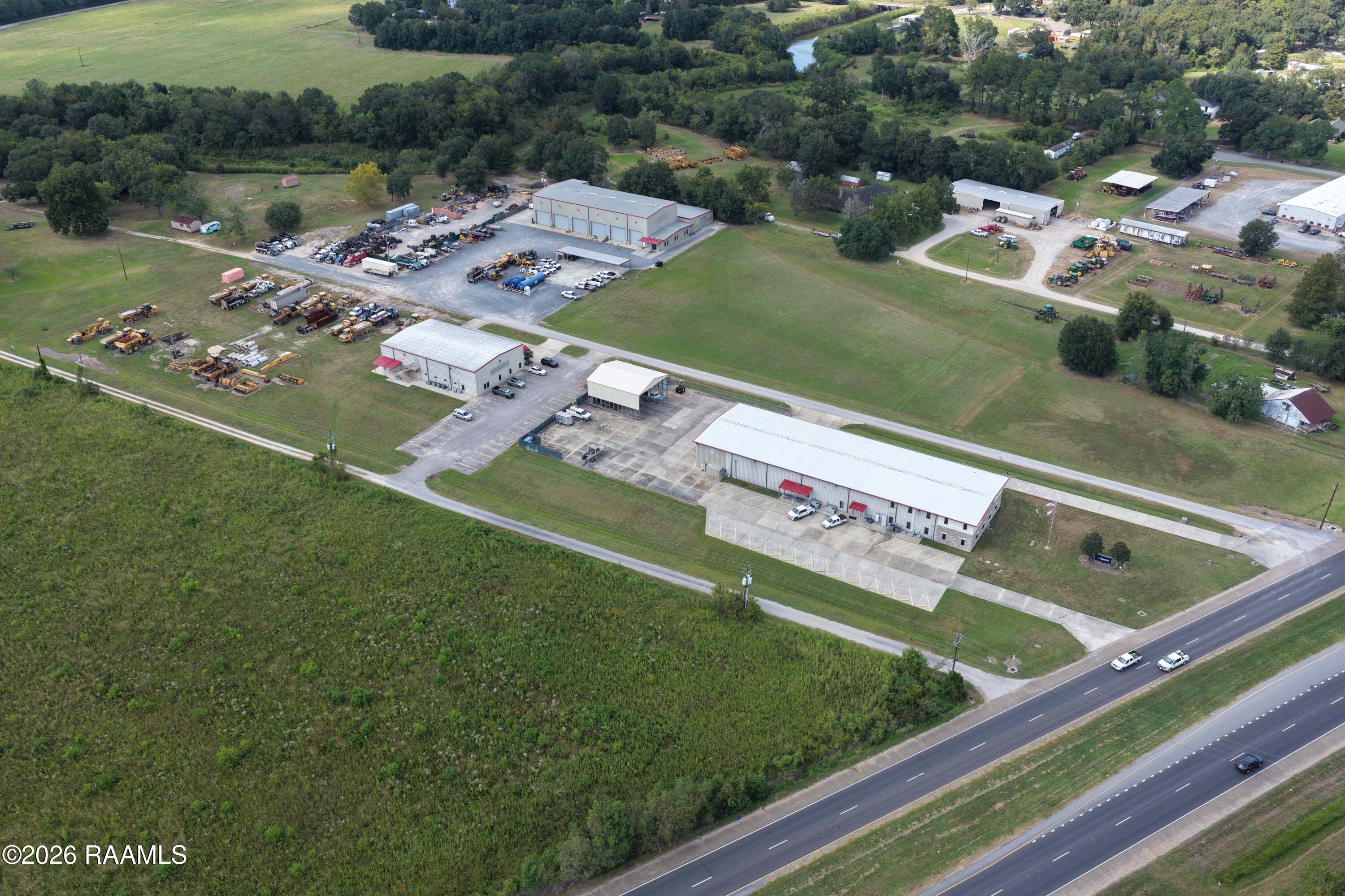 Aerial view of an equipment yard with industrial buildings, machinery, and highway frontage.