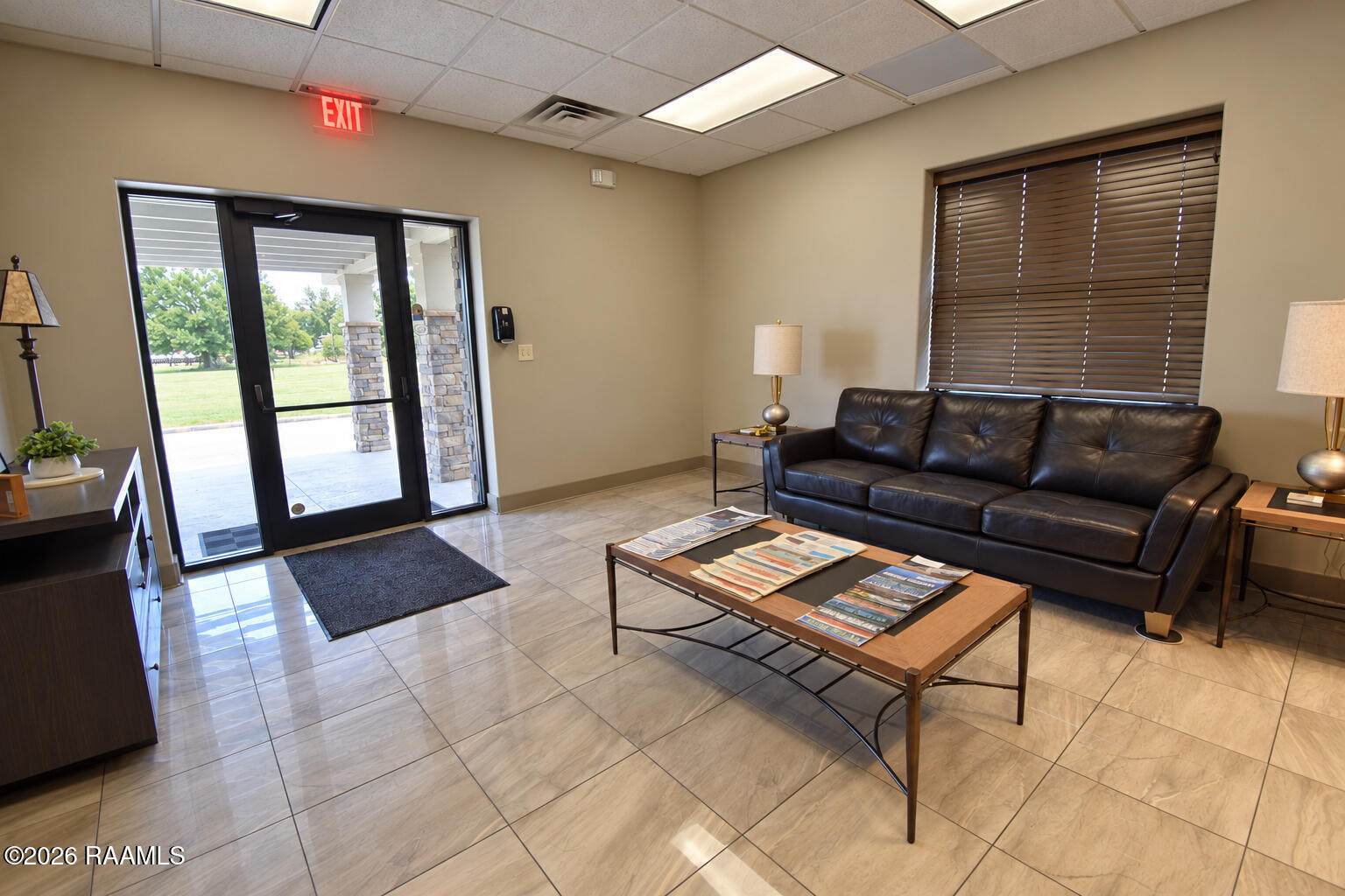 Furnished office lobby with a black leather sofa, tiled floor, and glass entrance doors.