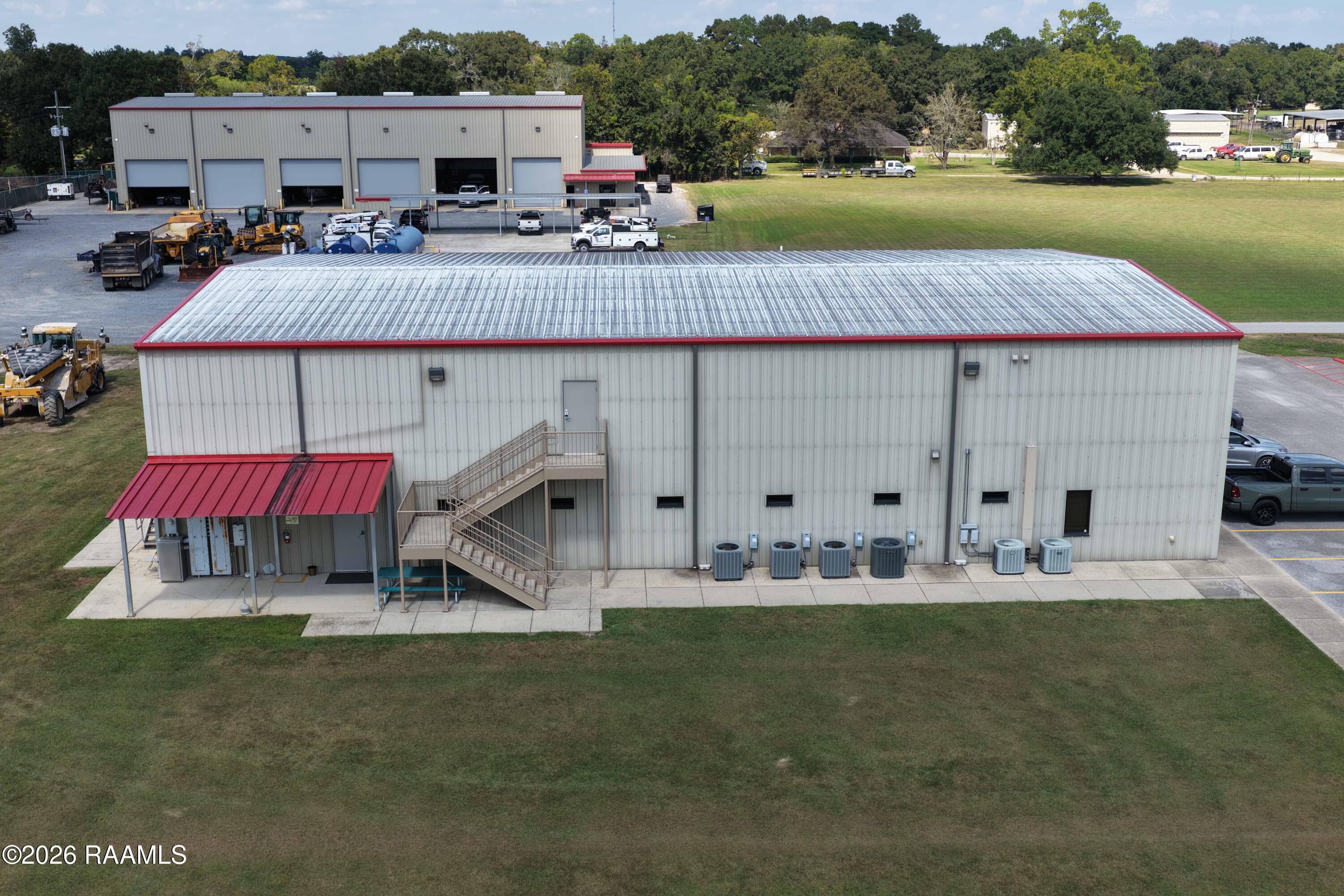 Aerial view of a metal warehouse with red roof trim, exterior stairs, and HVAC units.