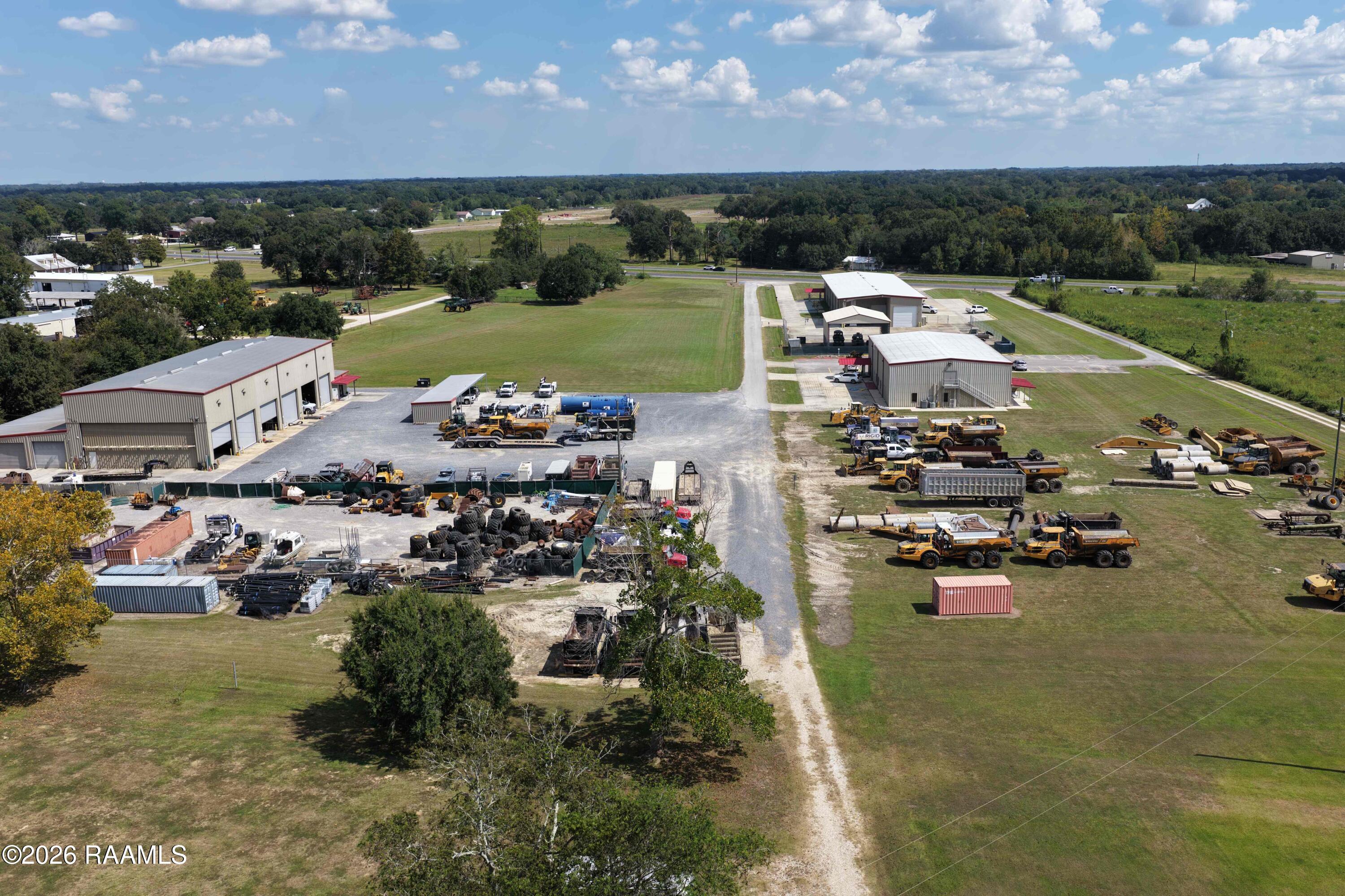 Aerial view of a commercial equipment yard with warehouses, heavy machinery, and gravel lots.