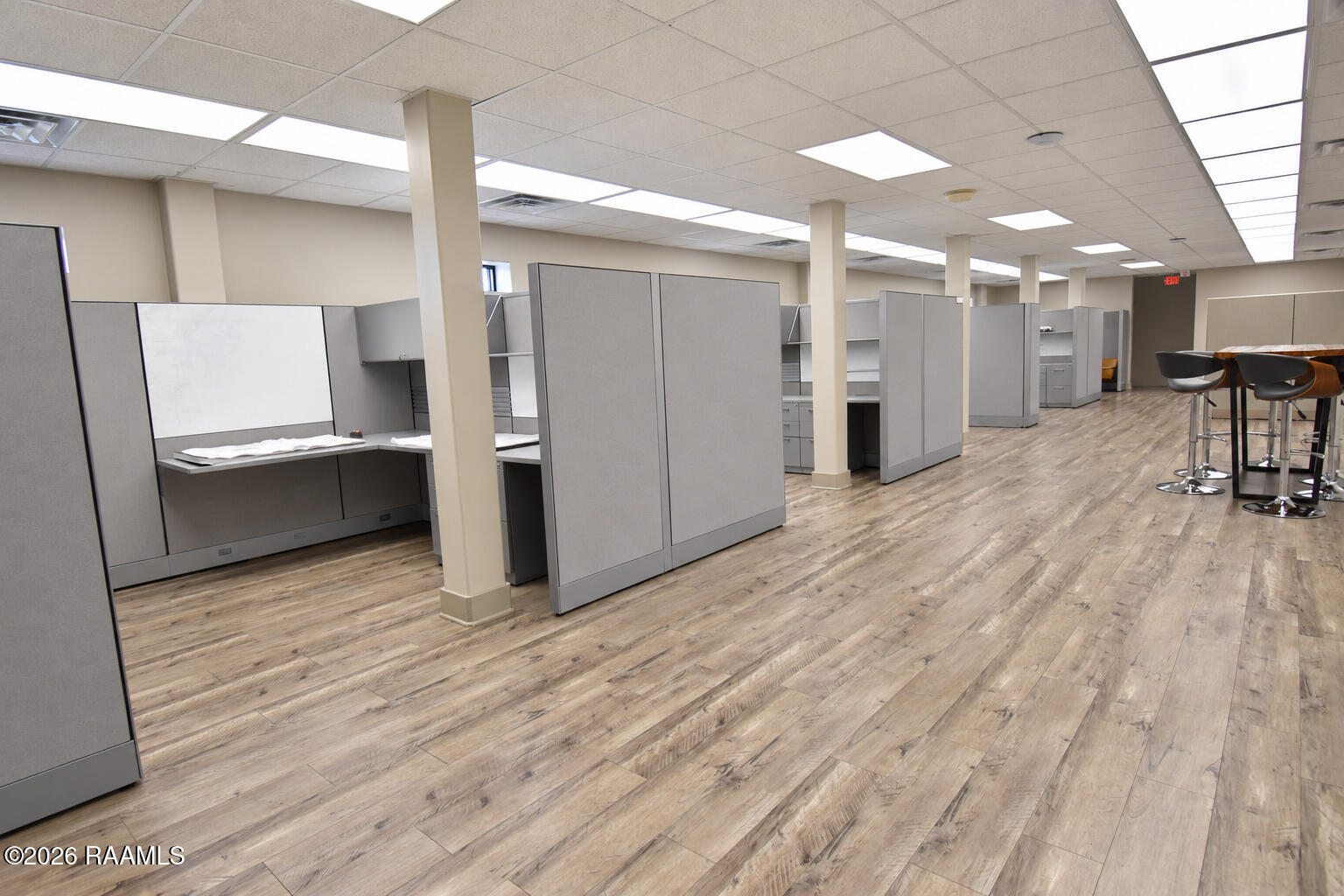 Open office with gray cubicles, wood-look flooring, and a counter-height table with stools.