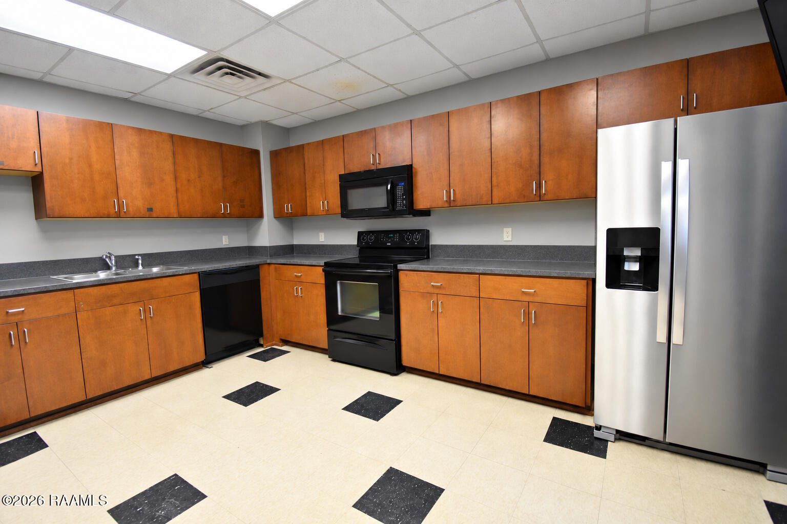 Kitchen with wood cabinets, gray counters, black appliances, and a stainless steel refrigerator.