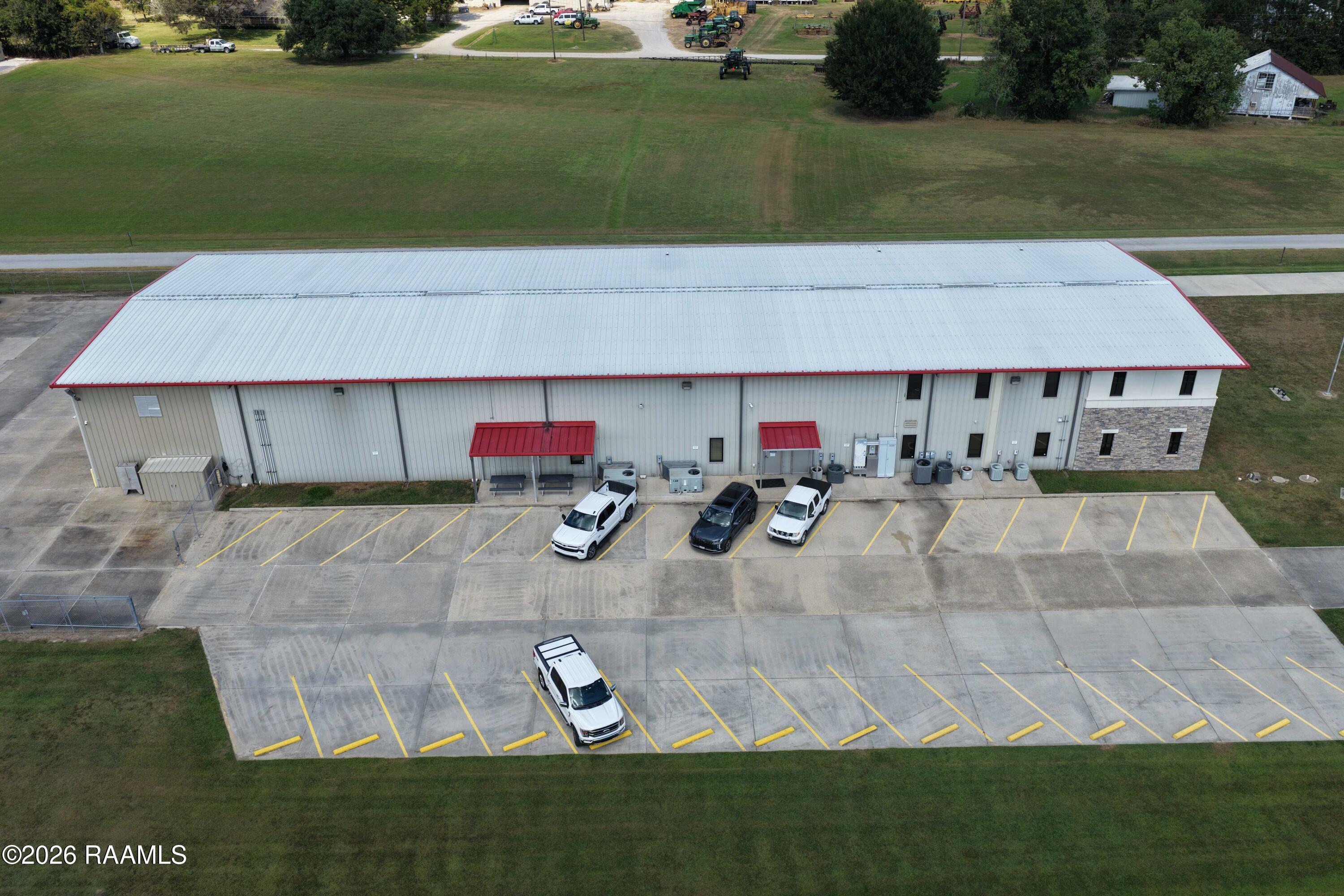 Aerial view of a long commercial building with red roof trim, parking lots, and grassy grounds.