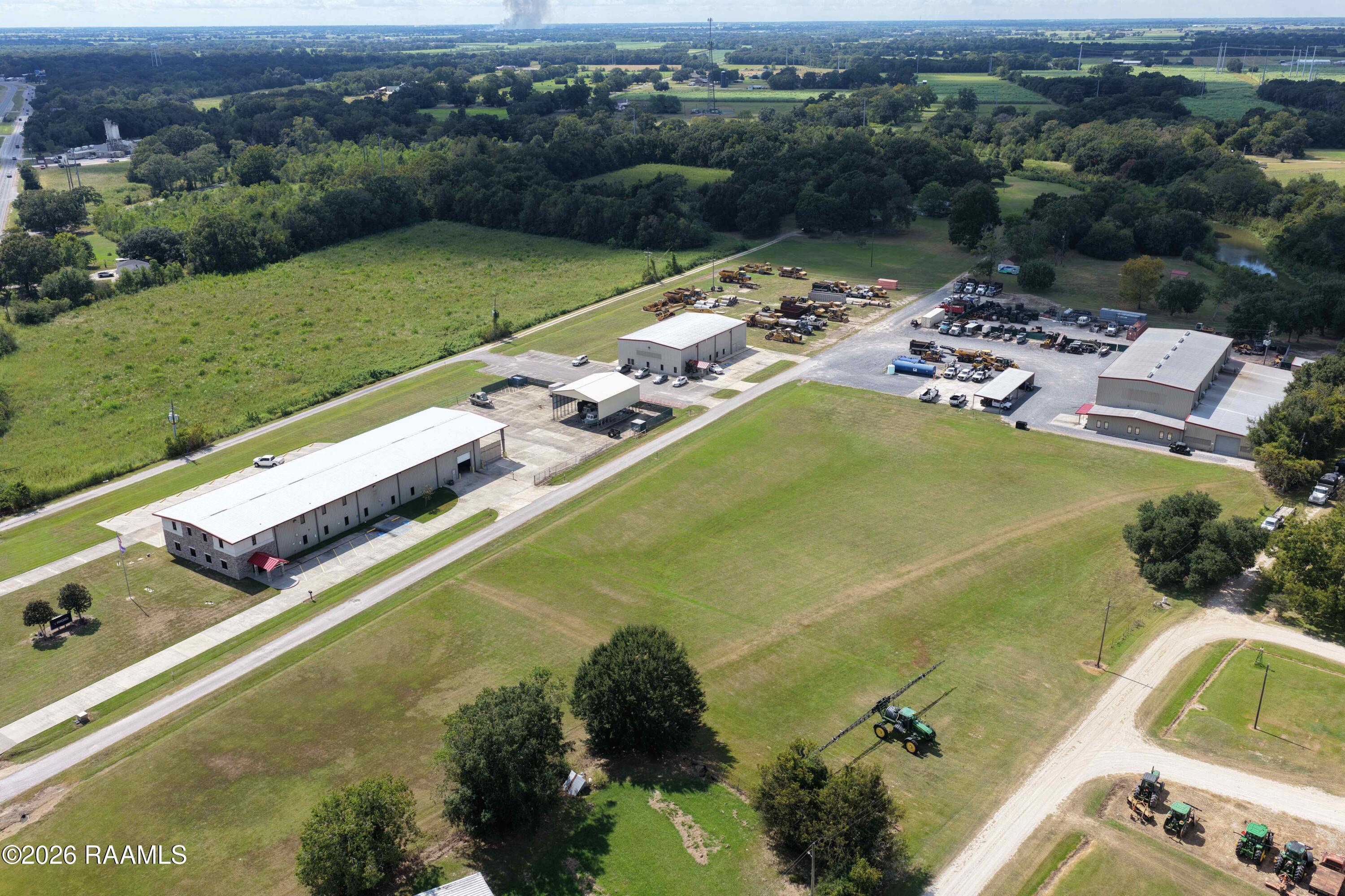 Aerial view of a commercial property with warehouse buildings, equipment yards, and broad grassy acreage.