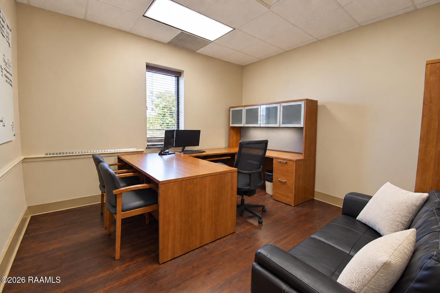 Furnished office with a large wooden desk, built-in cabinets, and a black leather sofa.
