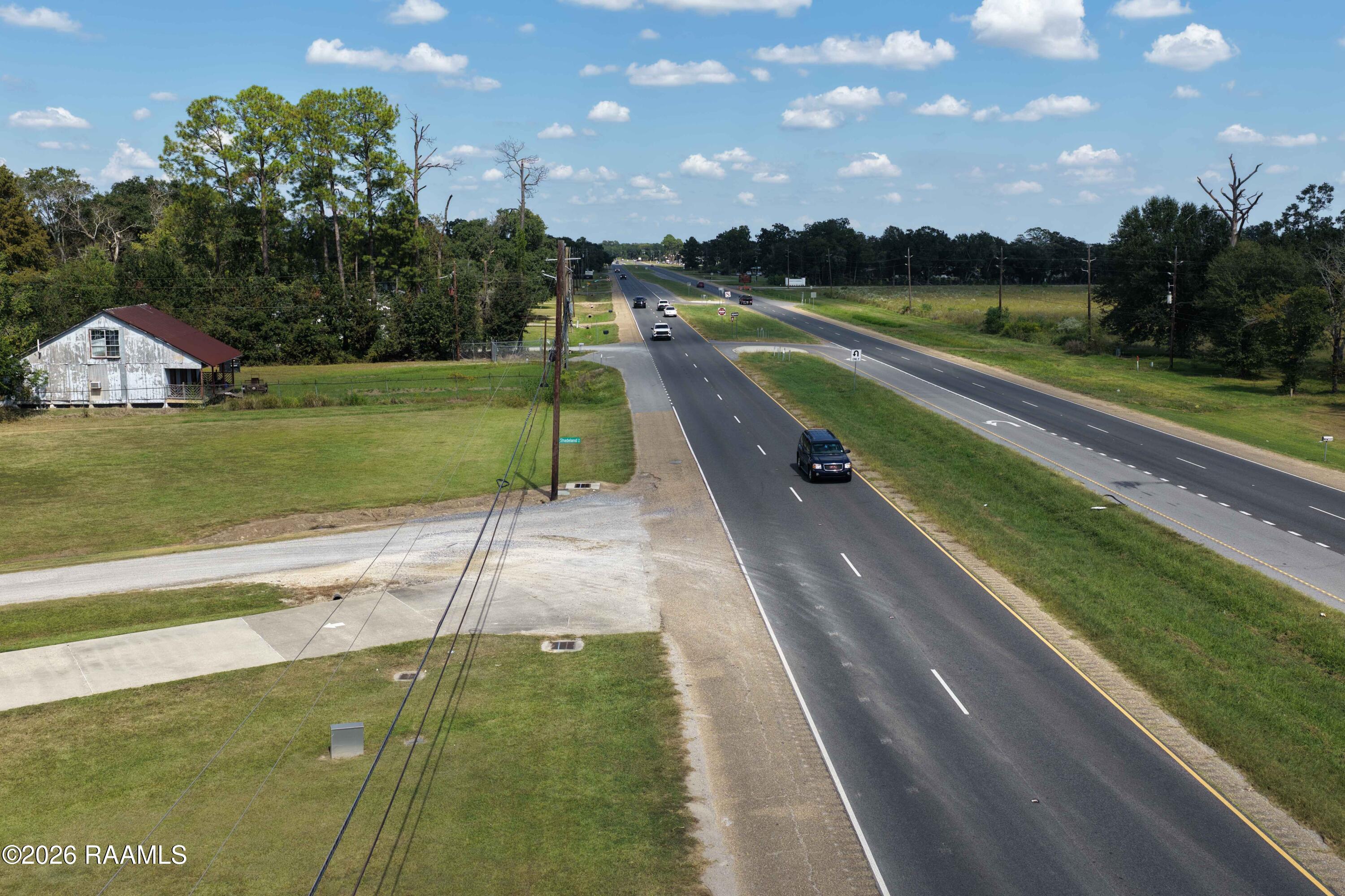 Grassy property beside a divided highway, with a gravel driveway and small weathered building nearby.