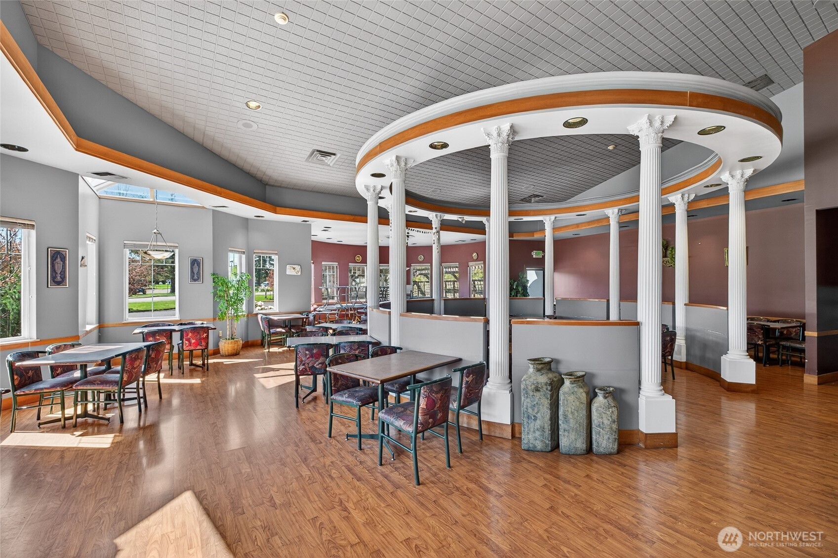 Dining room with patterned chairs, wood-look floors, and a curved ceiling feature with white columns.