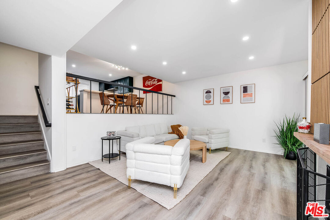 Living room with white seating, gray wood-look floors, and a raised dining area.