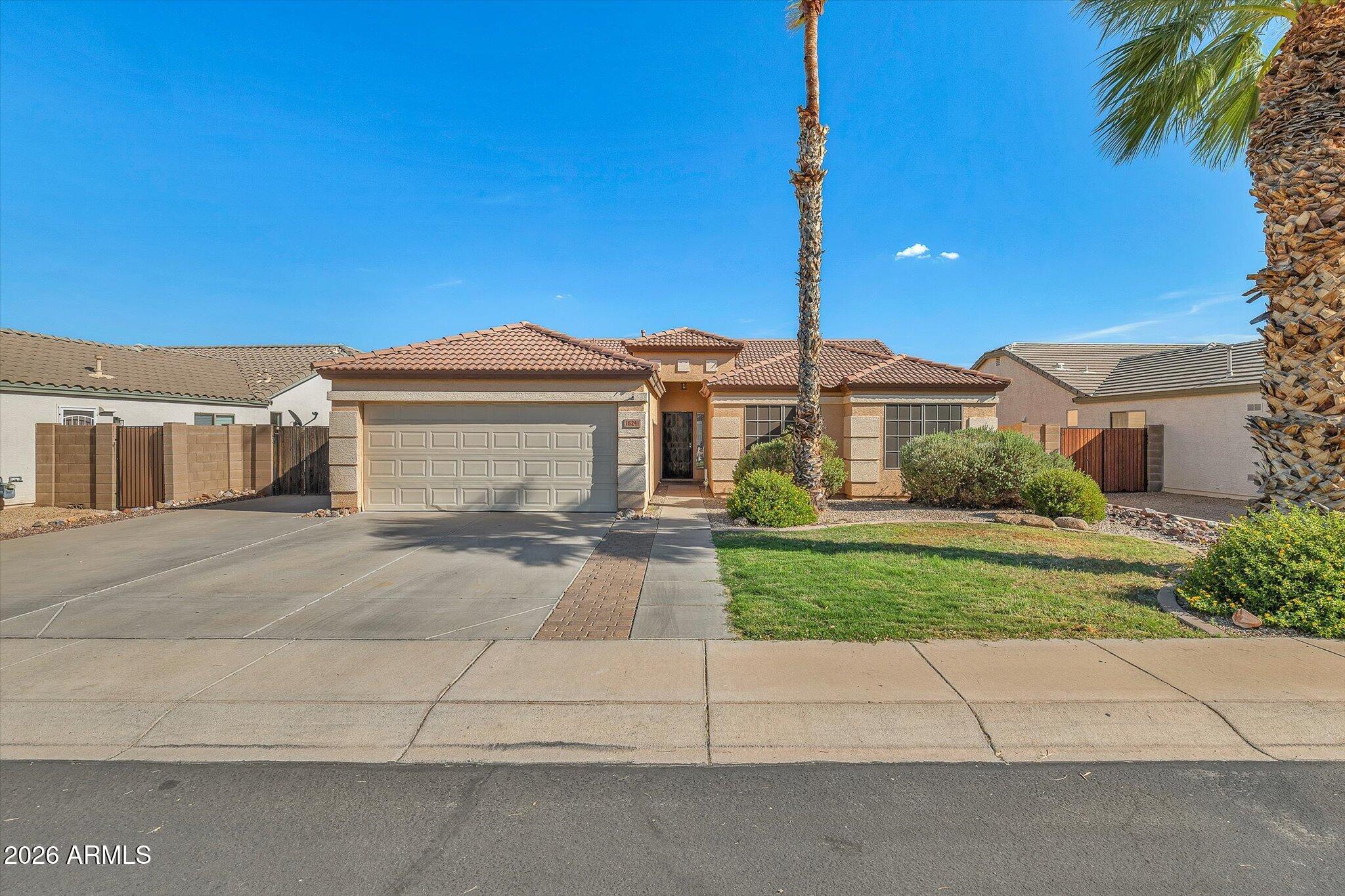 Single-story stucco home with a tile roof, two-car garage, palm trees, and a green front lawn.