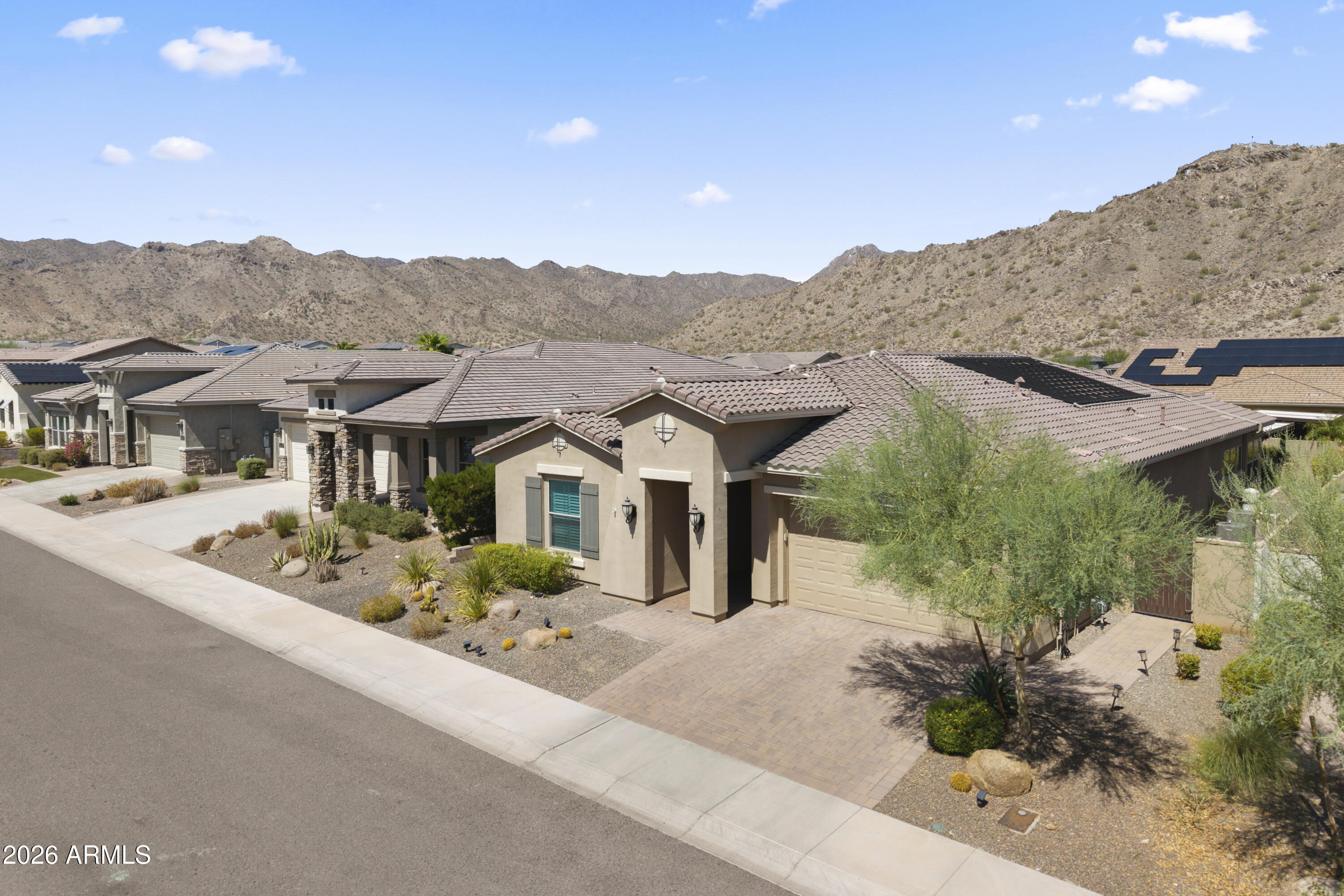 Tan stucco home with a tiled roof and desert landscaping, backed by rocky mountains.