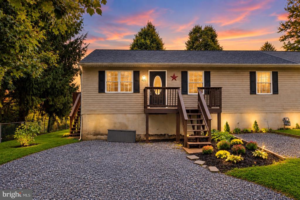 Beige raised ranch with elevated wooden entry decks, stairs, and a wide gravel driveway at dusk.