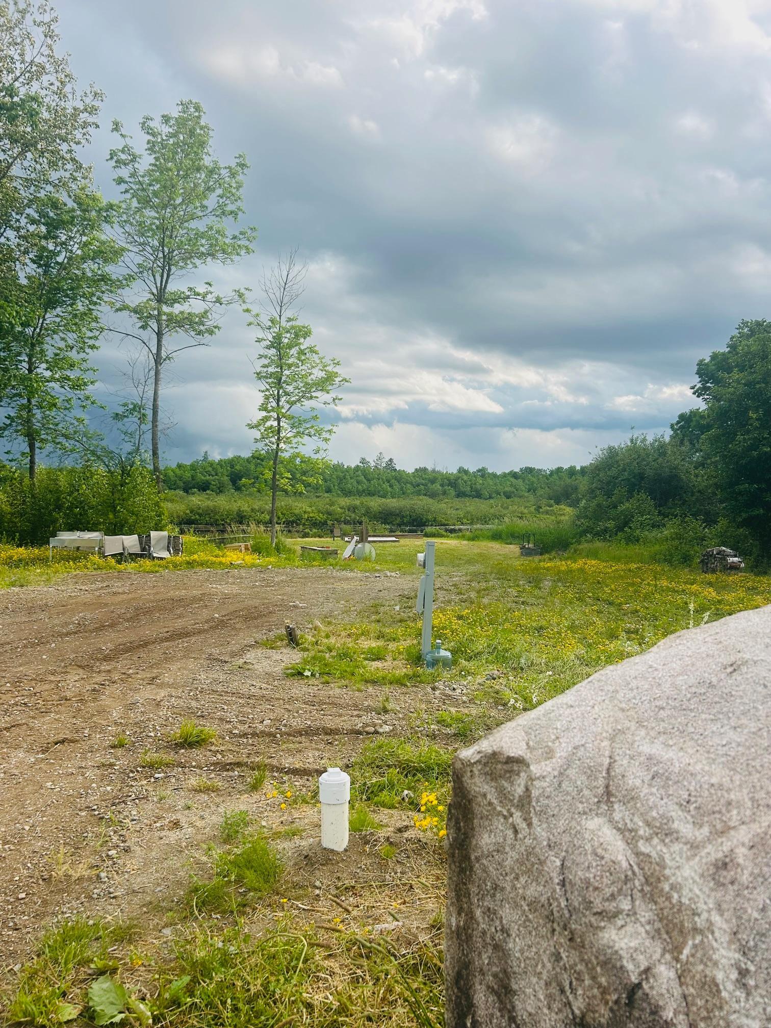 Partly cleared lot with utility hookups and a large foreground boulder, bordered by trees.