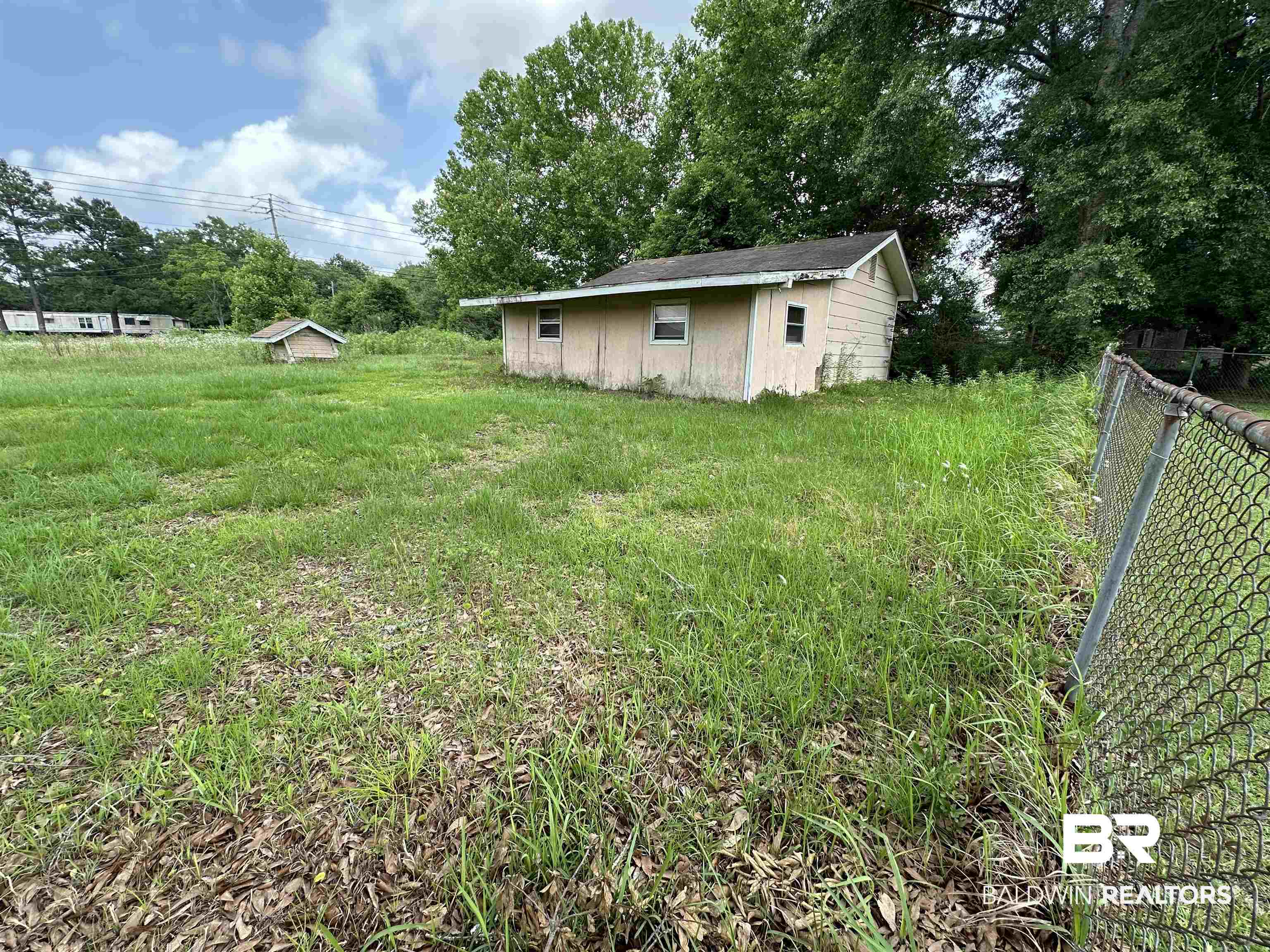 Small single-story building on an overgrown lot, with a chain-link fence along the right side.