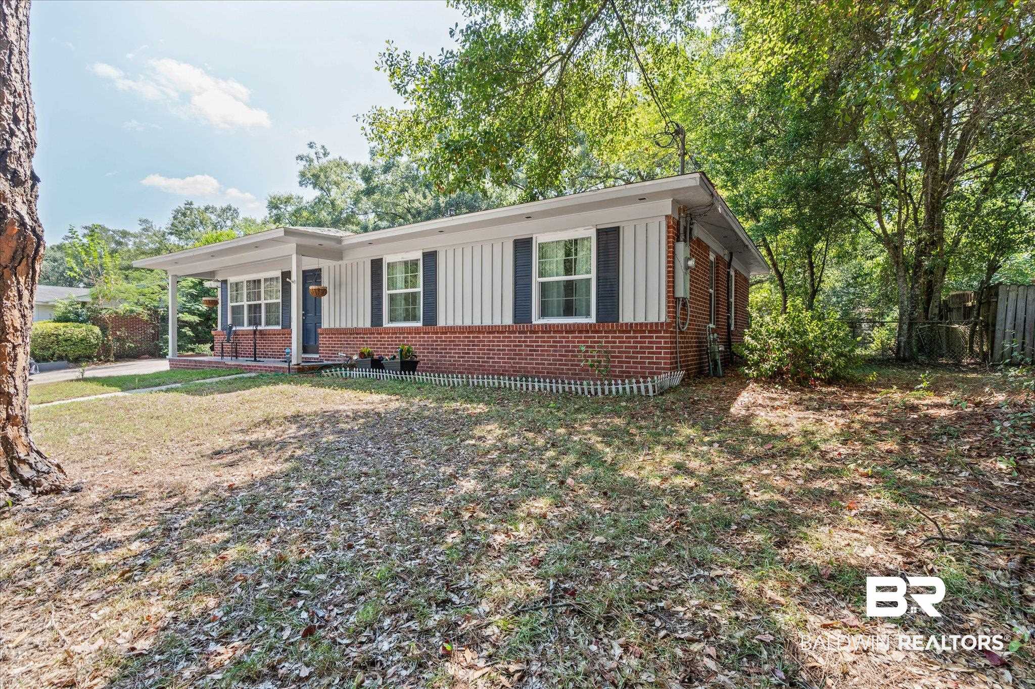 Single-story brick home with white siding, a covered porch, and a shaded, leaf-strewn yard.