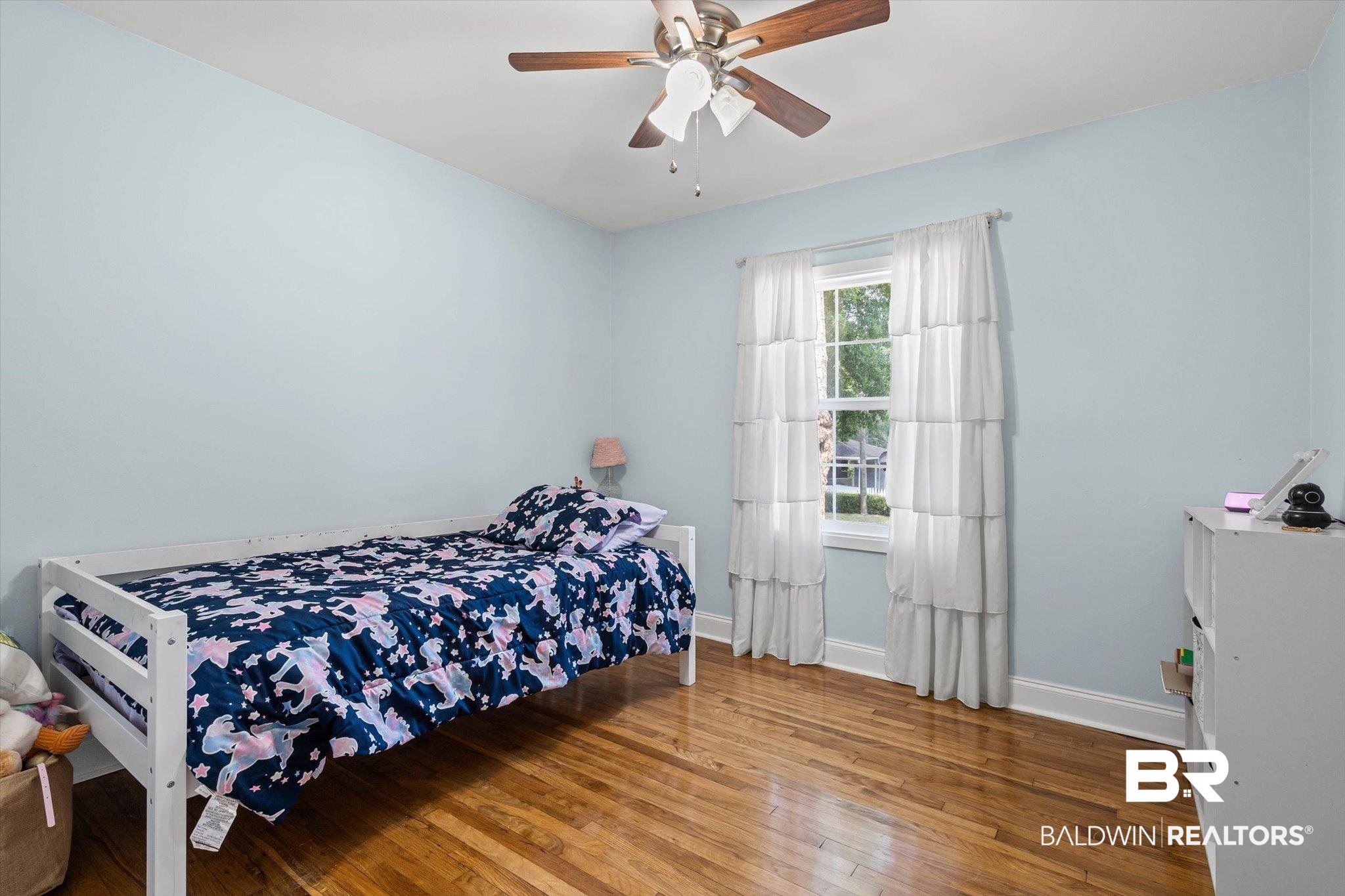Bedroom with navy unicorn-patterned bedding, pale blue walls, and hardwood floors.