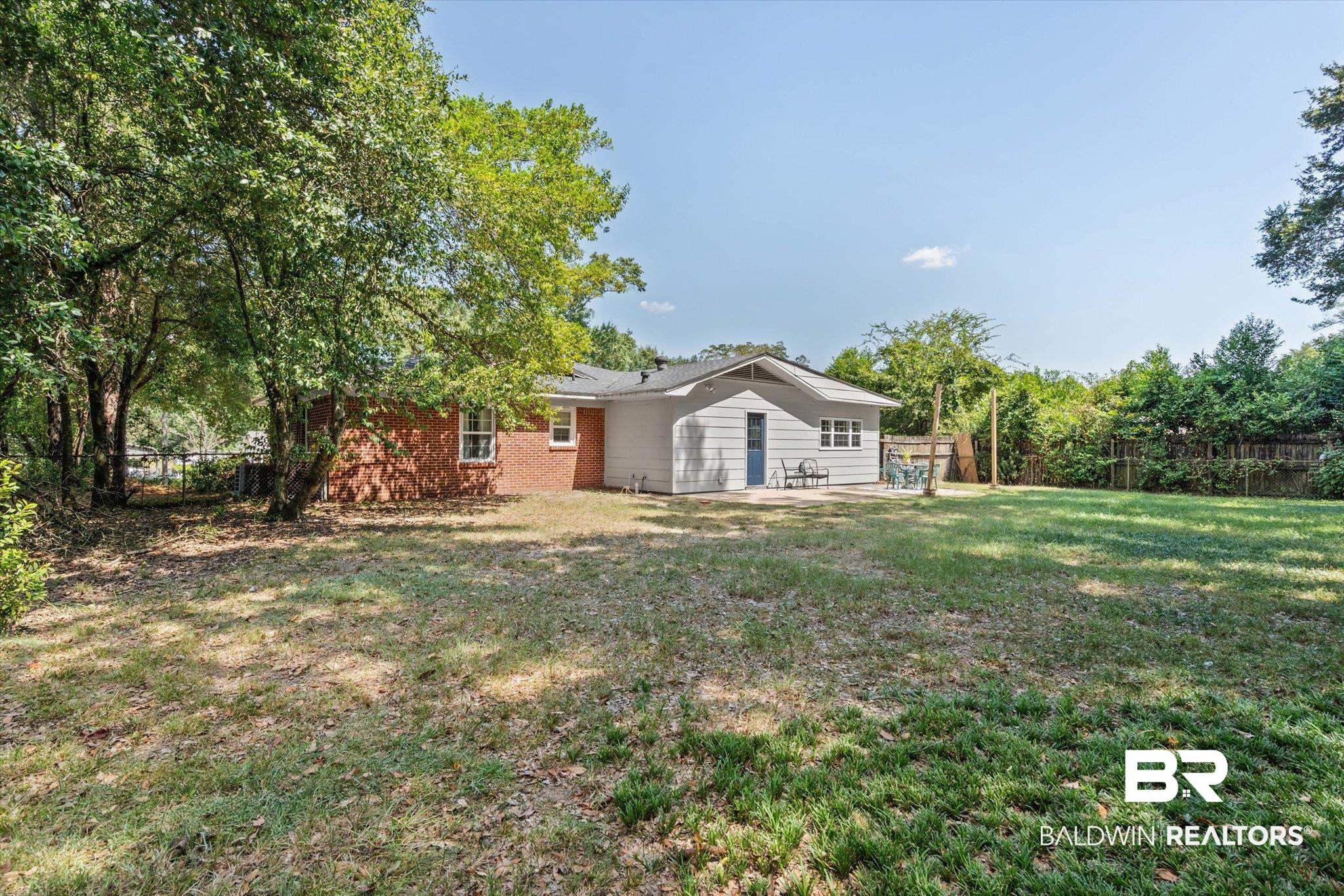 Rear of a brick-and-siding home with a shaded grassy backyard and small patio.