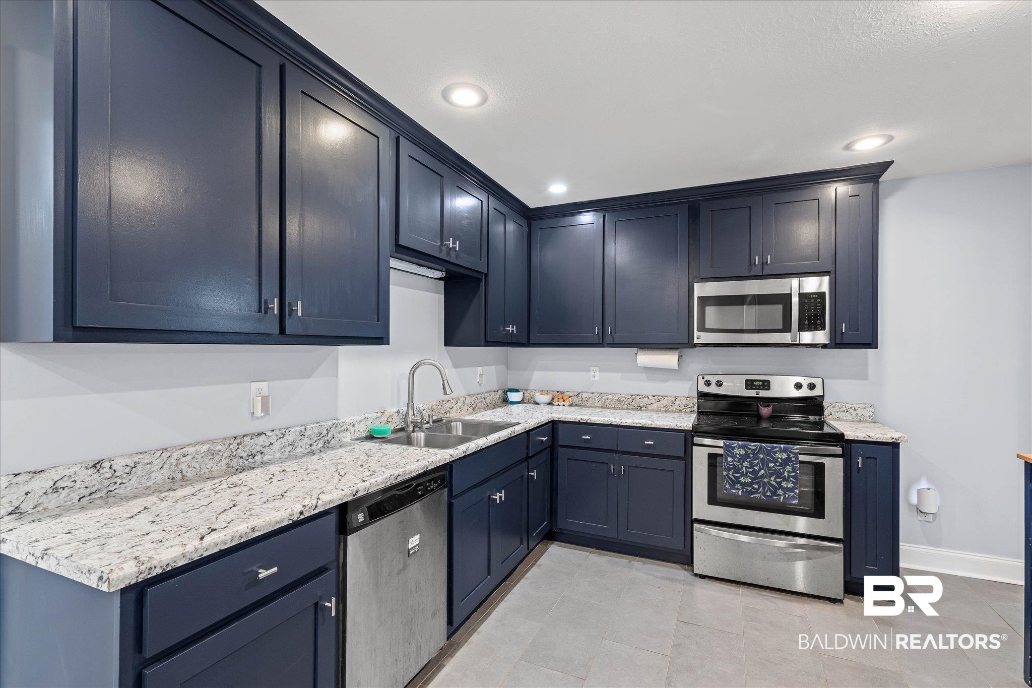 Kitchen with navy cabinets, marble-patterned counters, stainless steel appliances, and gray tile flooring.