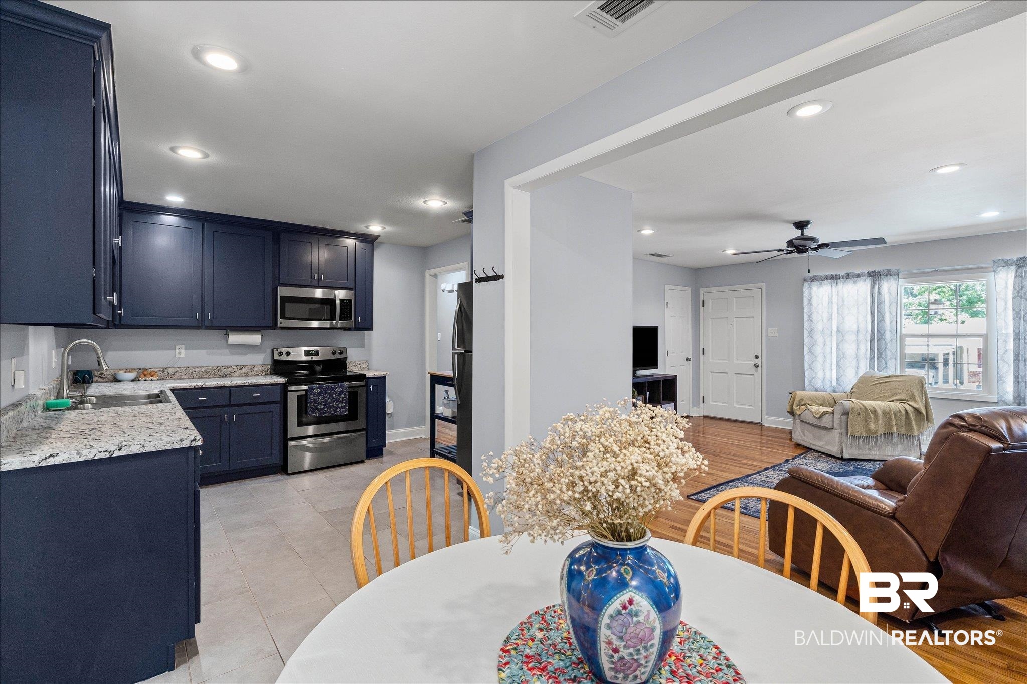 Open-concept kitchen and living room with navy cabinets, granite counters, and hardwood floors.