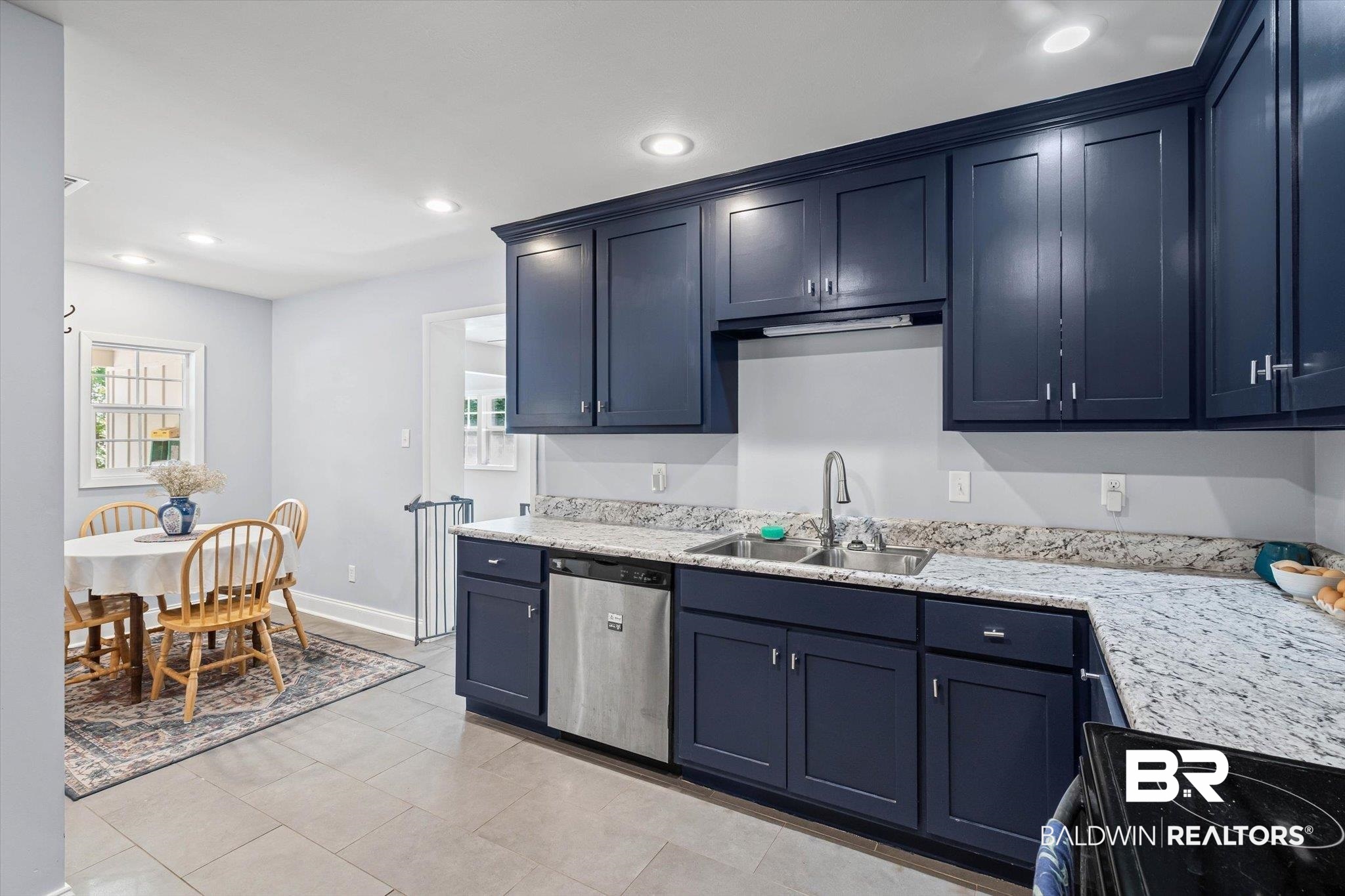Kitchen with navy cabinets, granite counters, stainless-steel dishwasher, and an adjoining dining table.