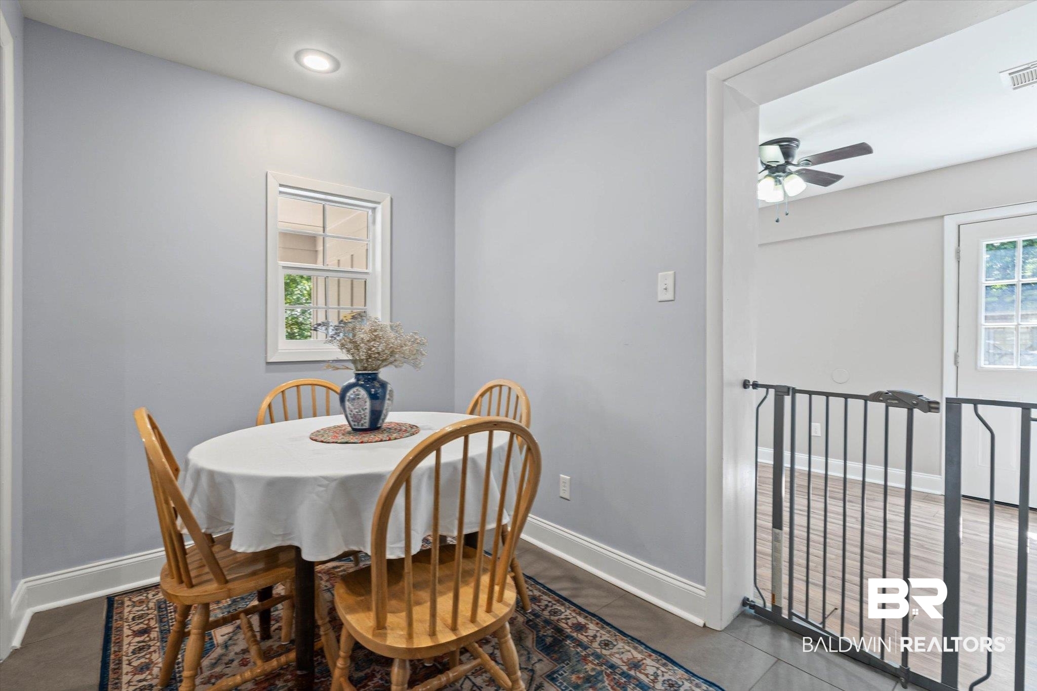 Dining area with a round table, wooden chairs, patterned rug, and safety gate to the adjoining room.