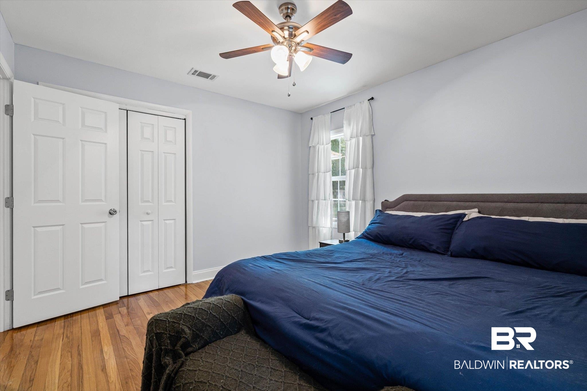 Bedroom with navy bedding, hardwood floors, white closet doors, and a ceiling fan.
