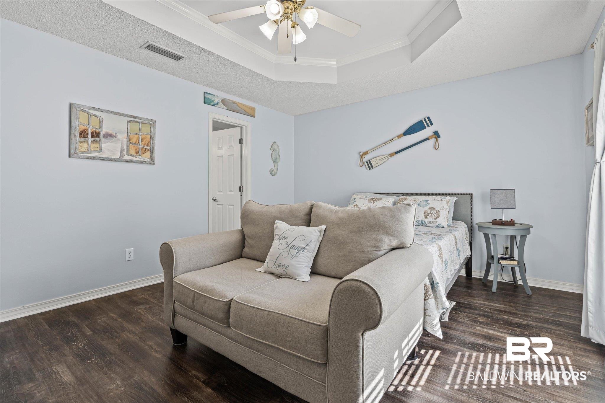 Furnished bedroom with a beige loveseat in front of a bed and coastal decor.
