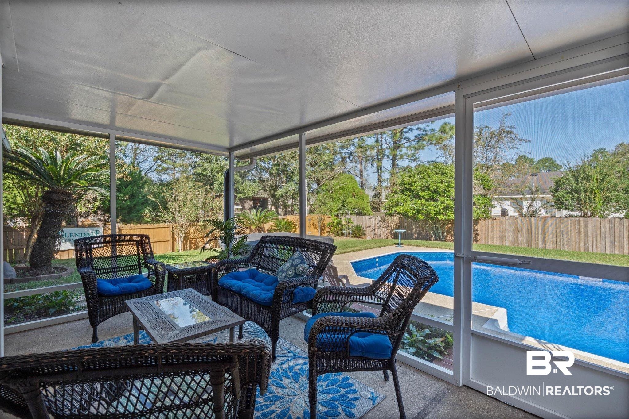 Screened patio with wicker seating and blue cushions overlooking a swimming pool.
