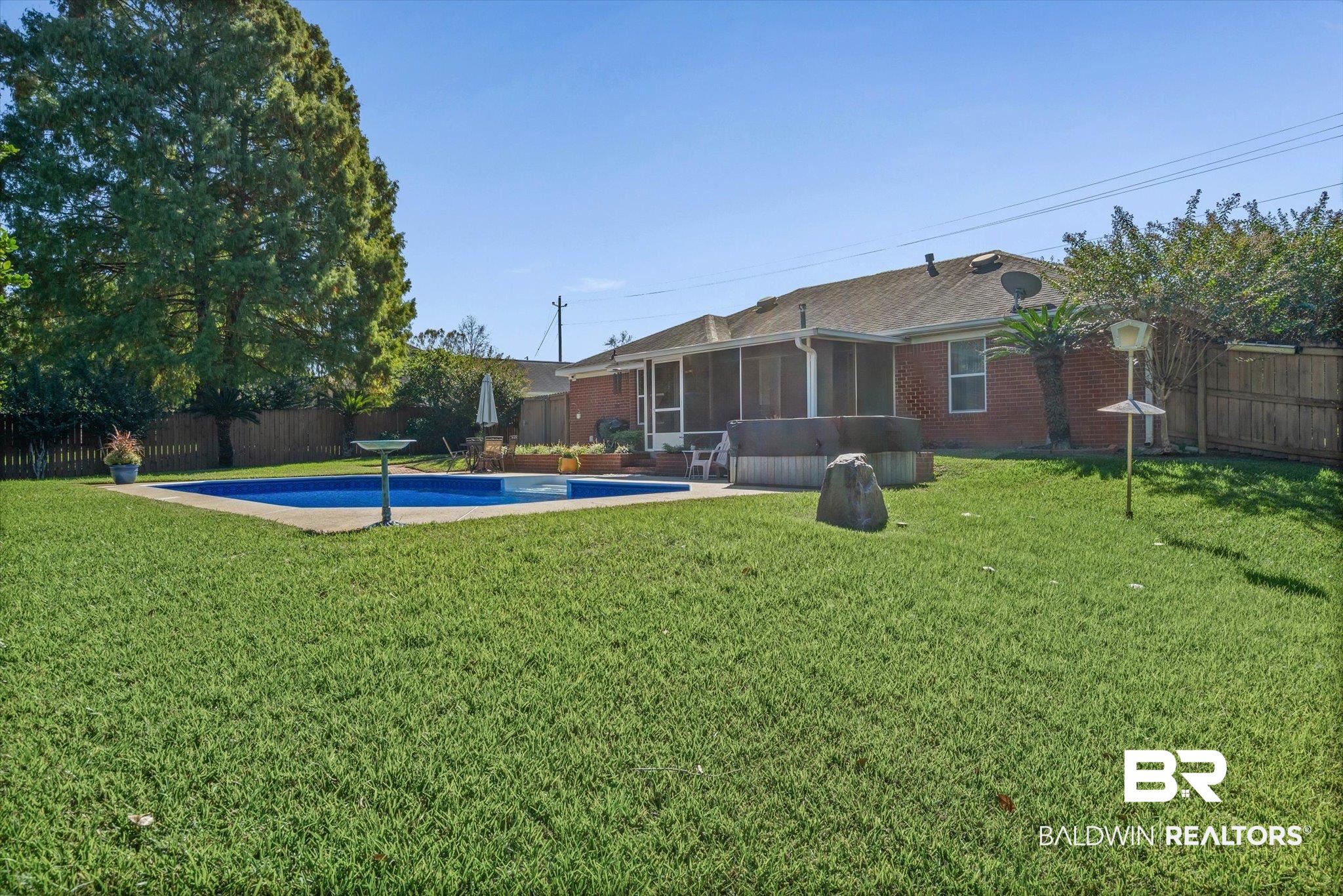 Brick home’s backyard with a screened porch, swimming pool, hot tub, and broad lawn.