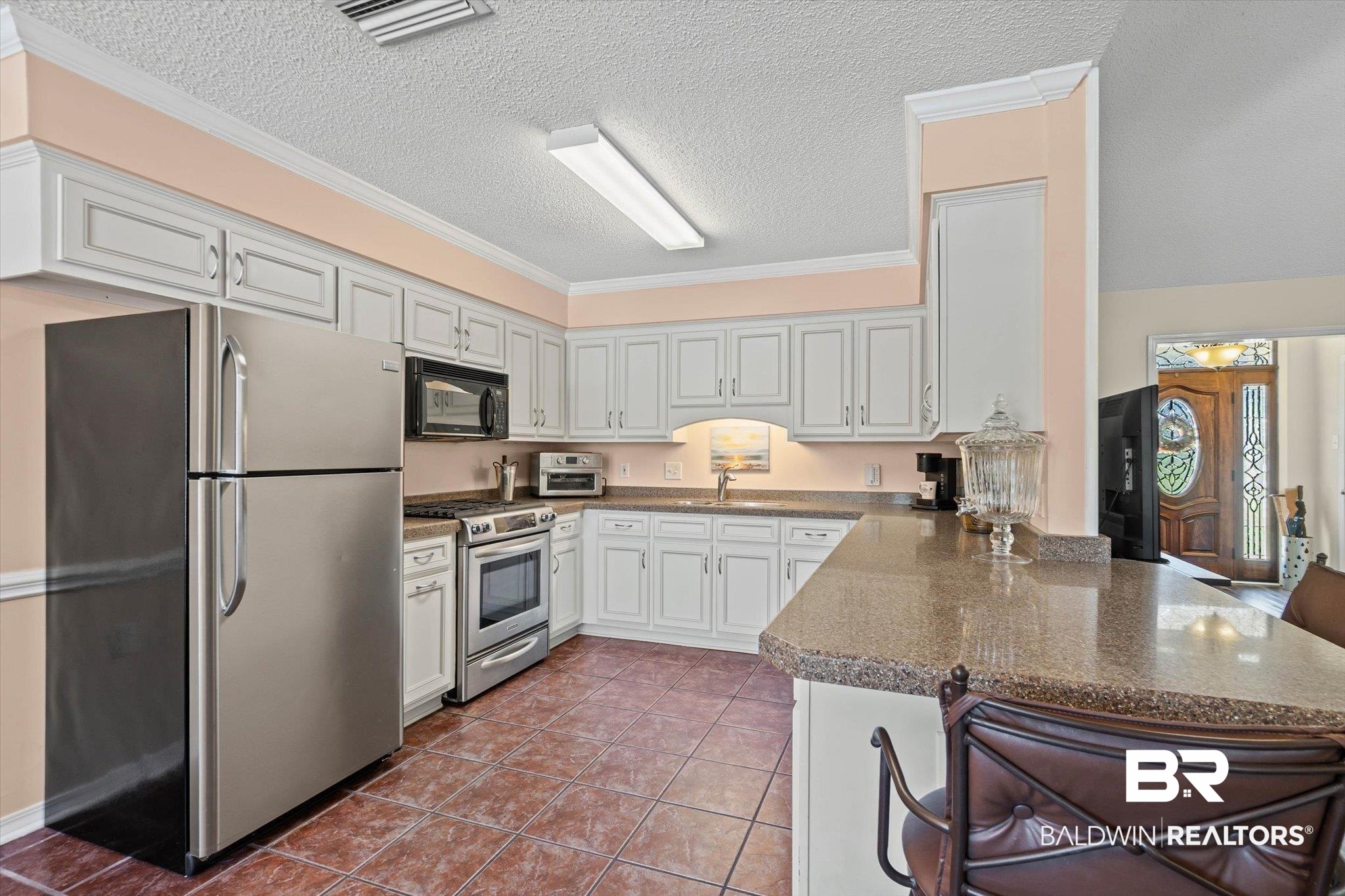Kitchen with white cabinets, stainless appliances, granite breakfast bar, and terracotta tile floor.