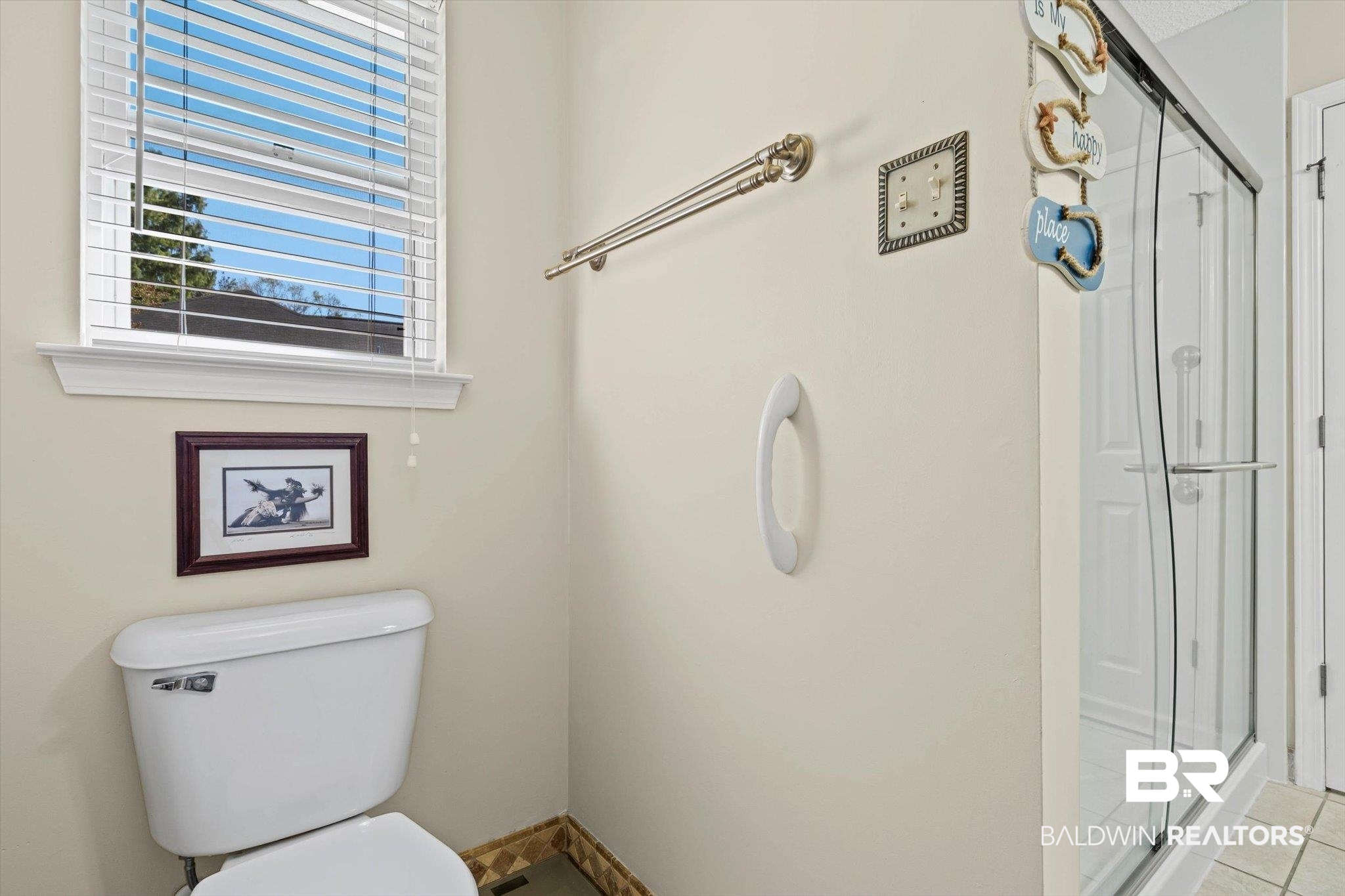 Bathroom with a glass-enclosed shower, toilet beneath a window, and wall-mounted grab bar.