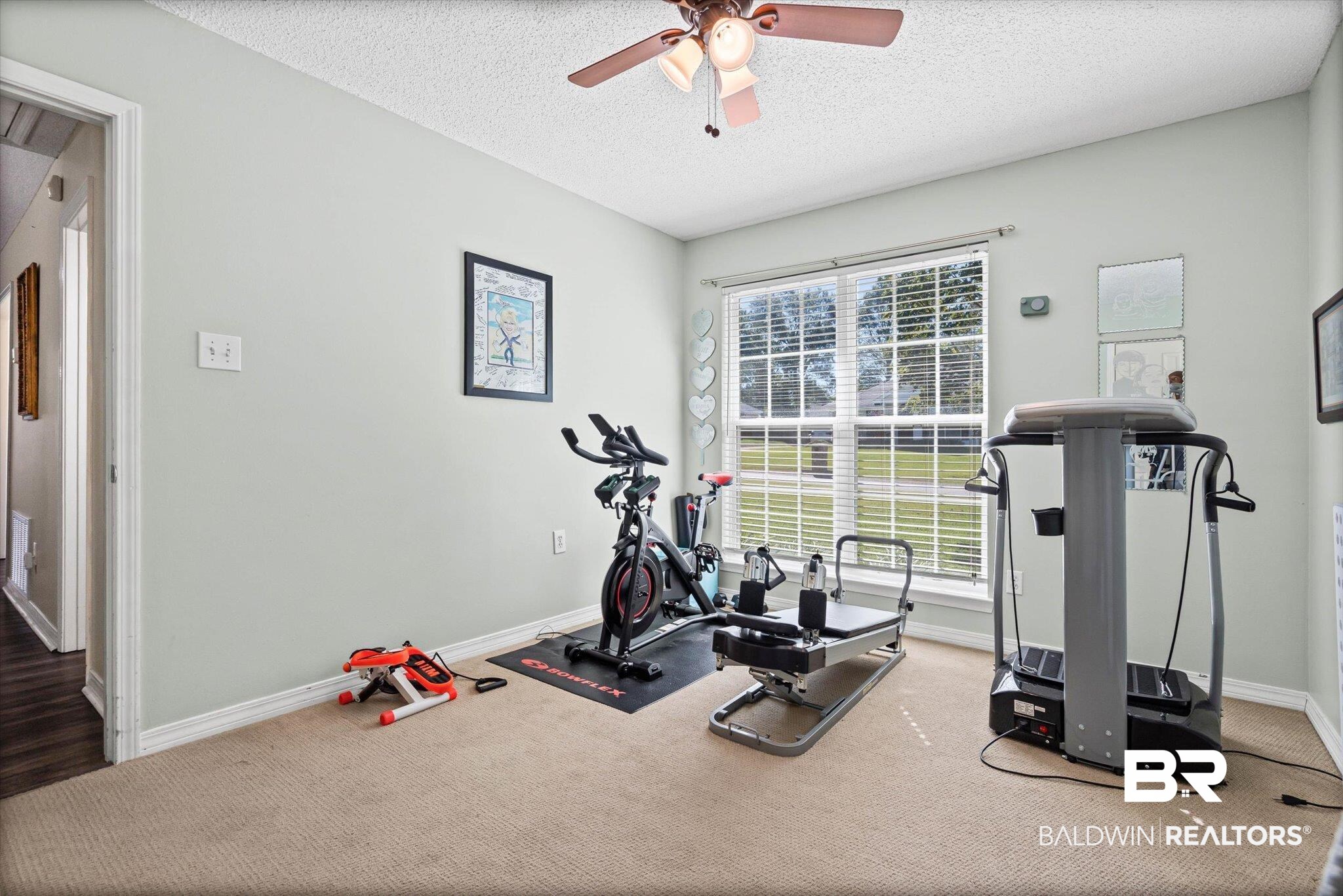 Home gym with an exercise bike, Pilates reformer, and treadmill beside a large window.