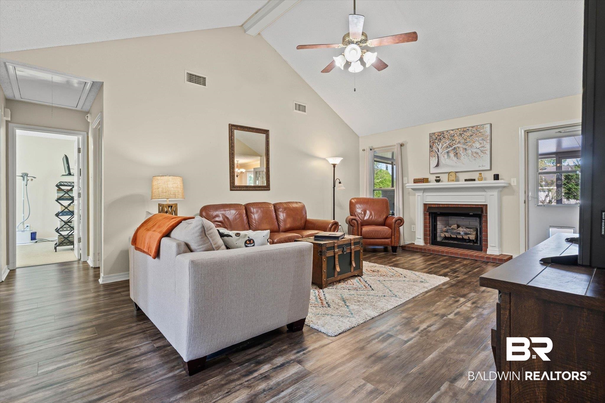 Living room with vaulted ceiling, leather seating, wood-look floors, and a white fireplace.