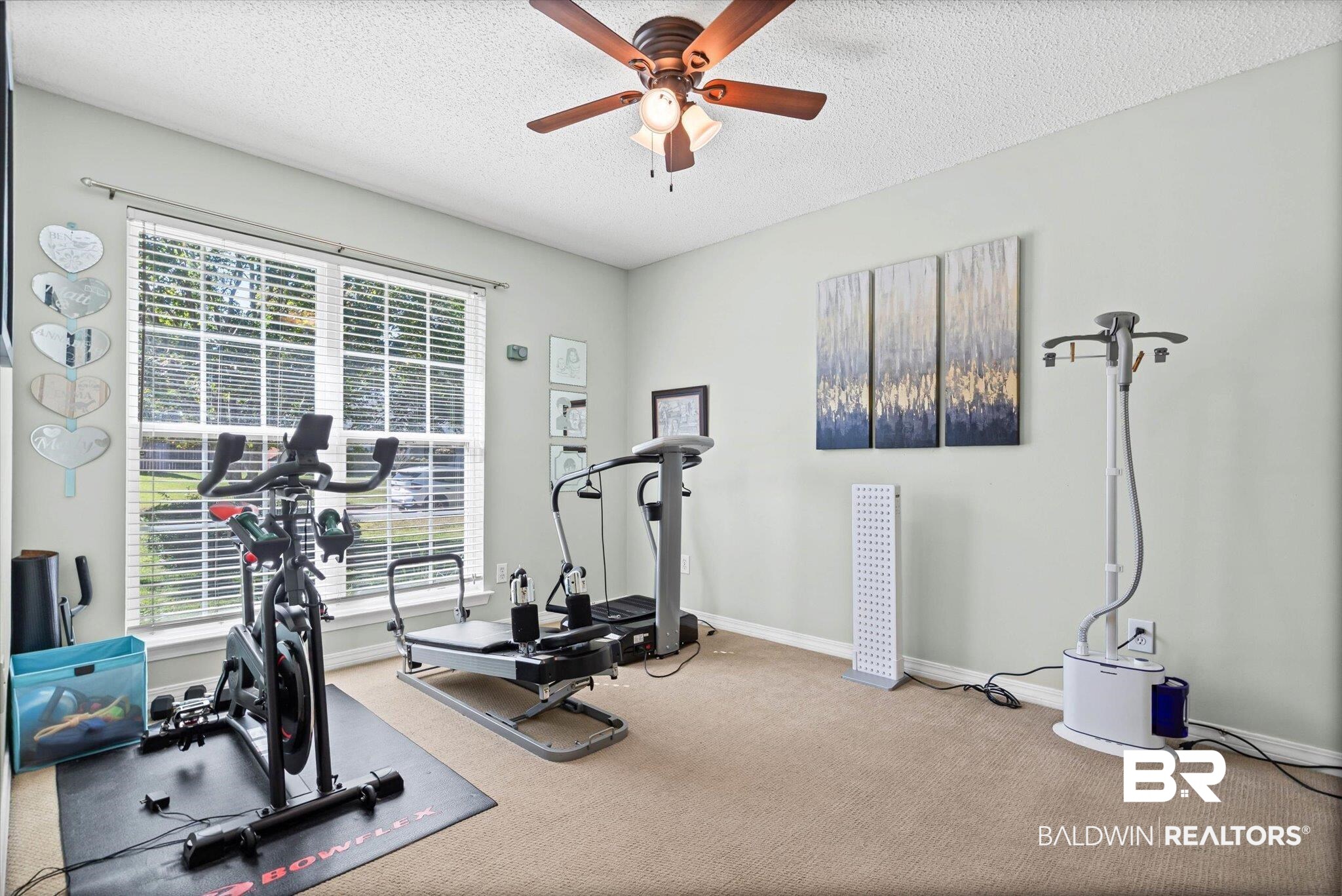 Home gym with Bowflex exercise equipment beside a large window with white blinds.