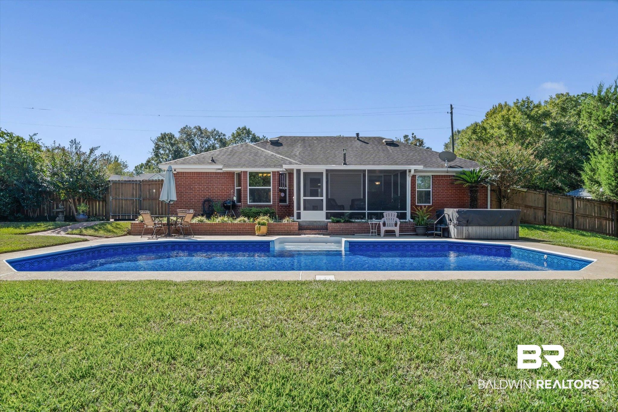 Brick home with screened porch behind a long swimming pool and fenced lawn.