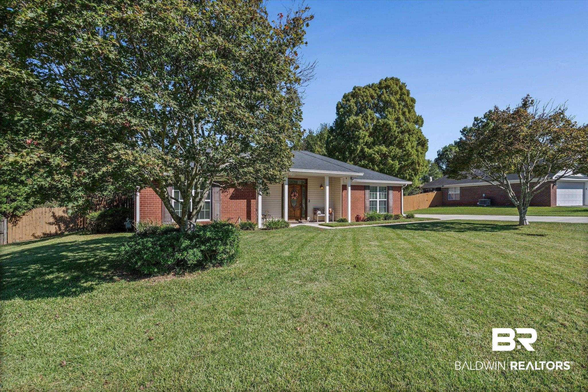 Single-story brick-and-siding home with covered entry, mature trees, and broad front lawn.