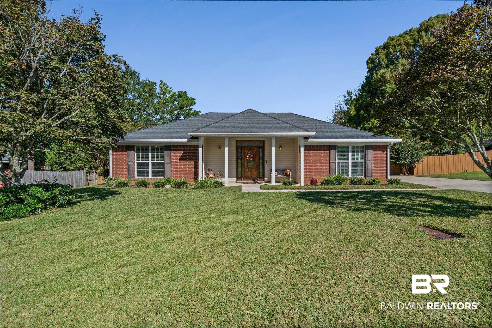 Single-story brick-and-siding home with a covered porch, broad lawn, and mature trees.