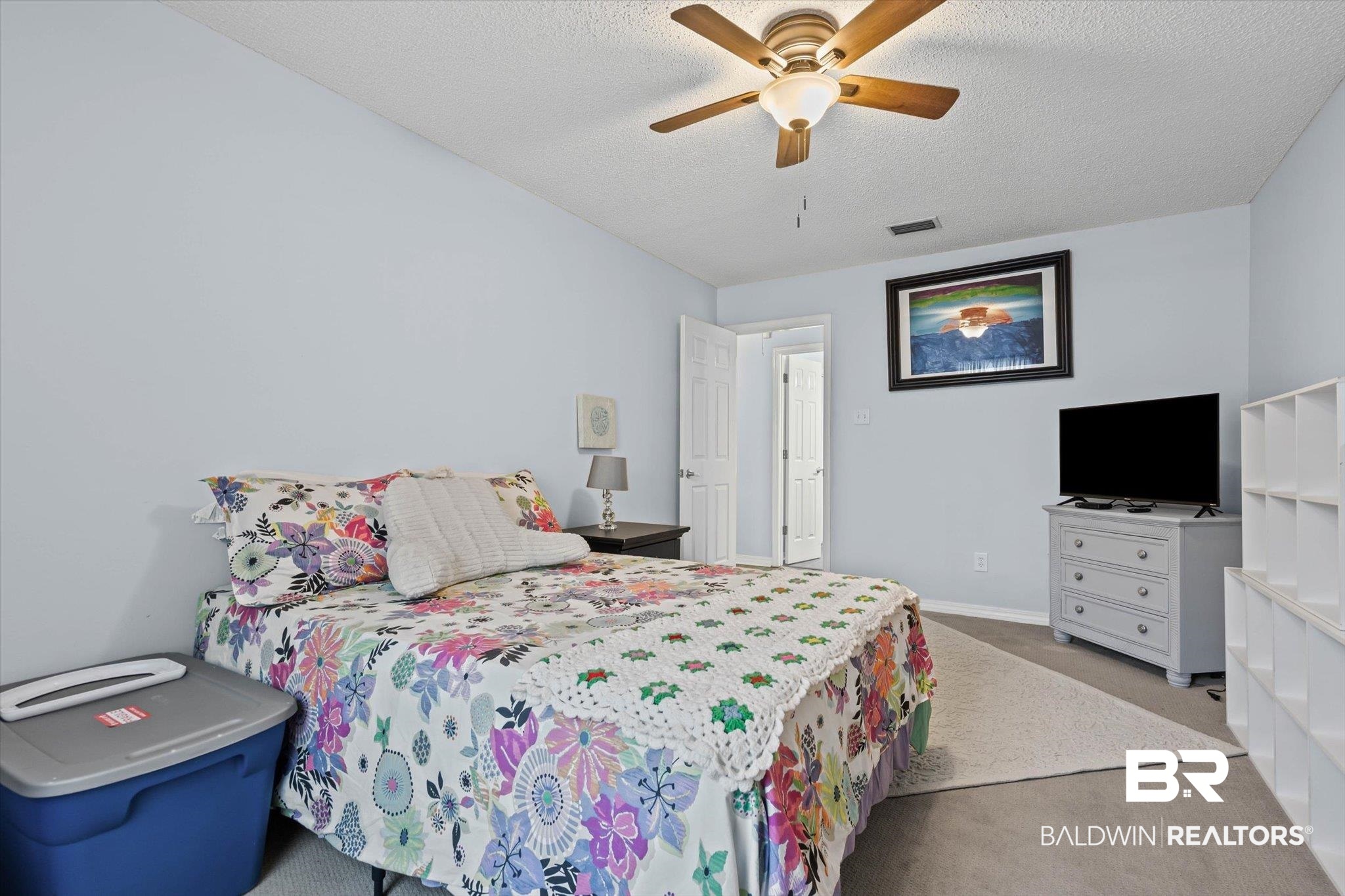 Bedroom with a colorful floral bedspread, crocheted blanket, and television on a dresser.