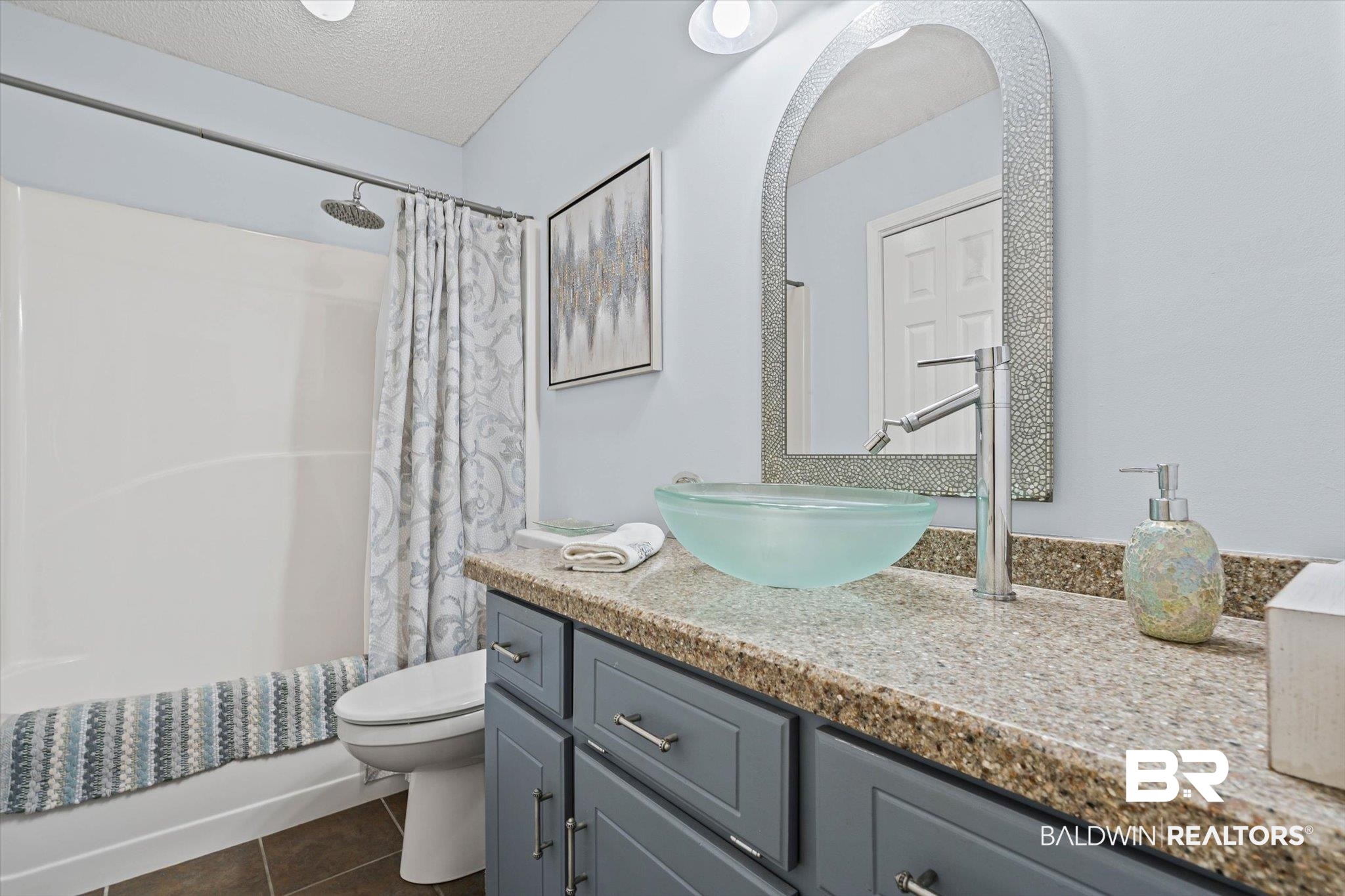 Bathroom with a pale aqua vessel sink, gray vanity, and white tub with patterned shower curtain.