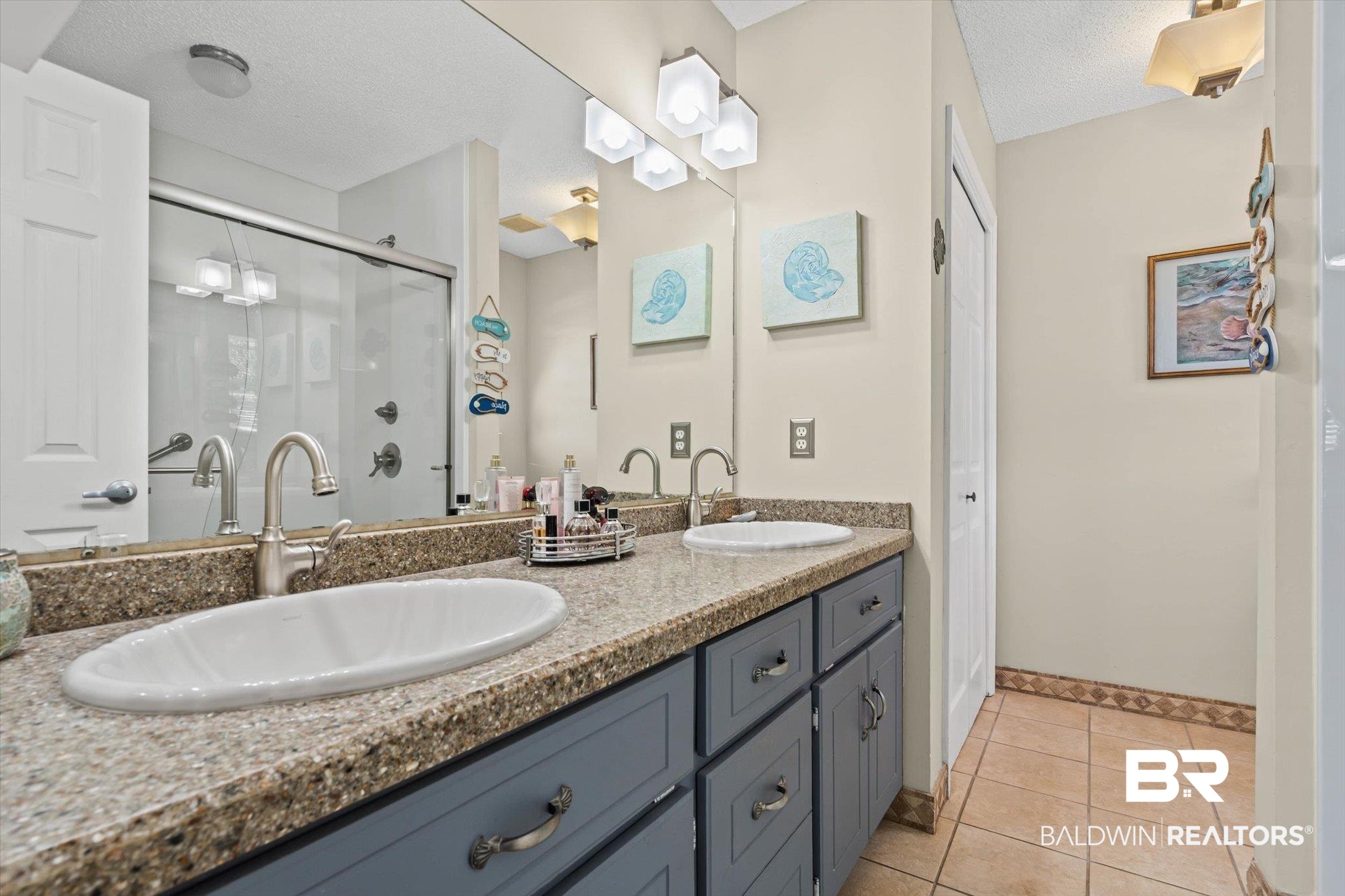 Bathroom with double sinks, gray vanity cabinets, and a glass-enclosed shower.