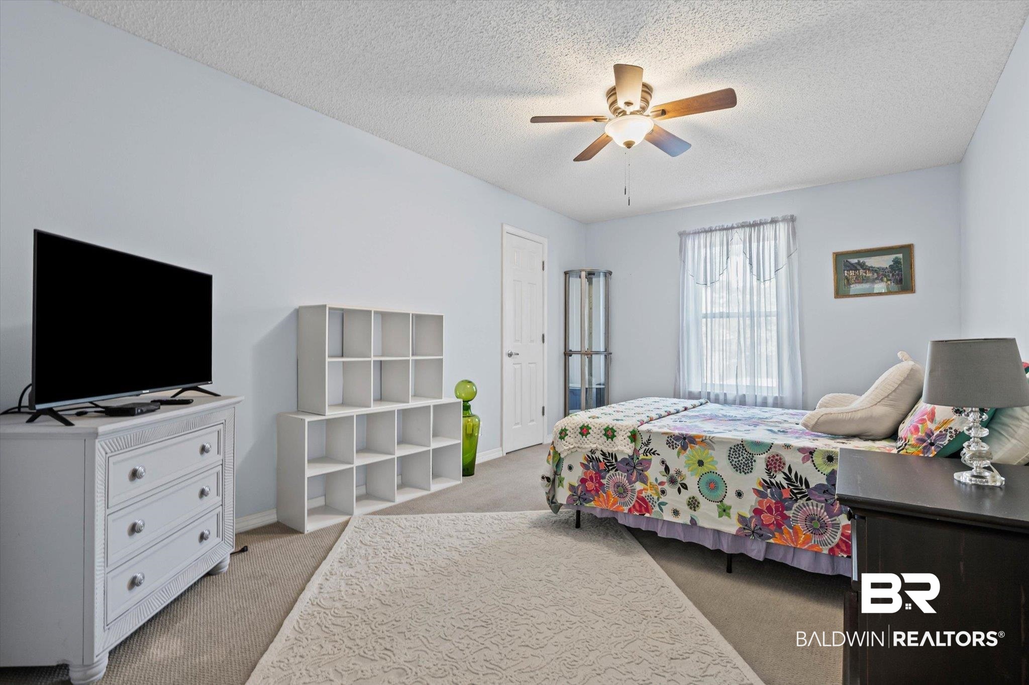Bedroom with a colorful floral bedspread, white cube shelving, and a ceiling fan.