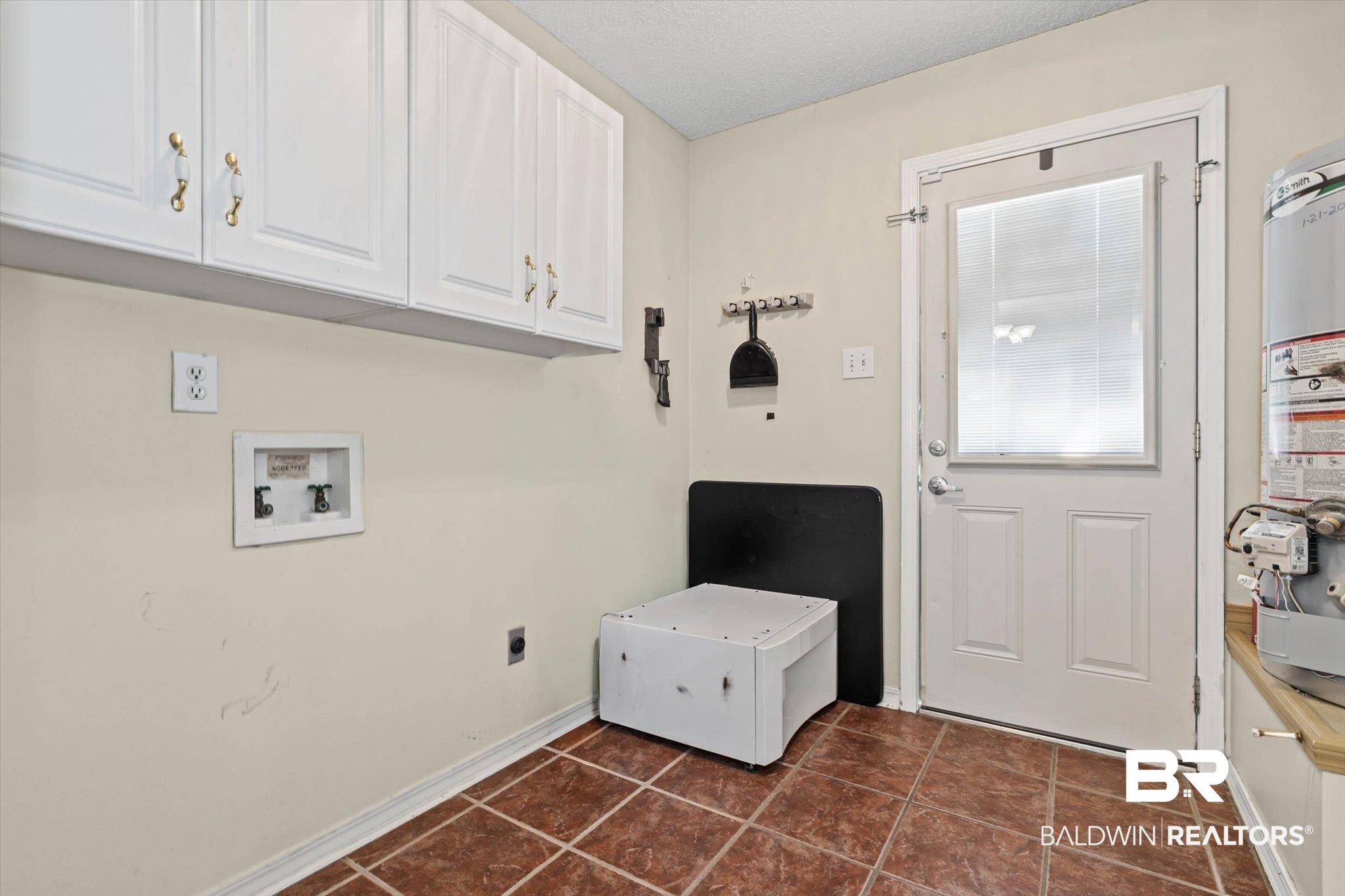 Laundry room with white cabinets, a washing machine, terracotta tile, and a windowed exterior door.