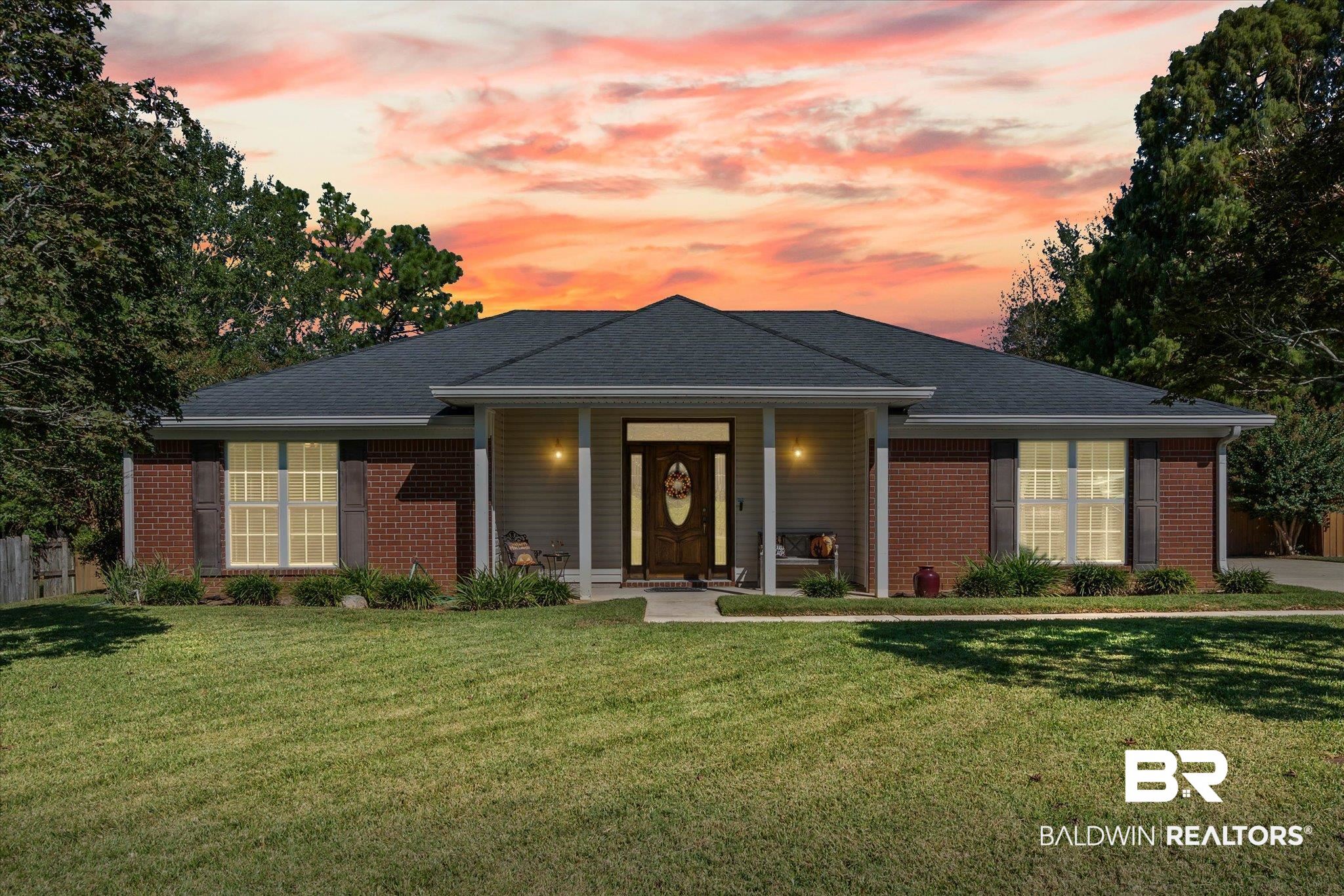 Single-story brick home with a covered entry and landscaped lawn beneath a vivid sunset.