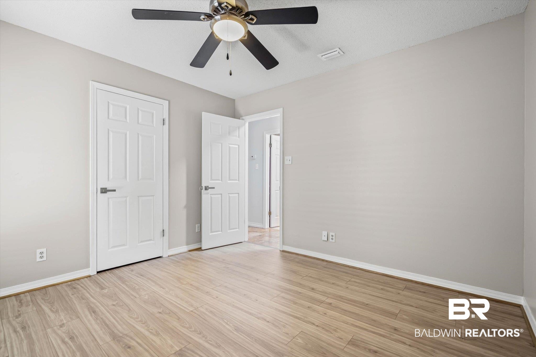 Empty room with light wood-look floors, a ceiling fan, and two white paneled doors.