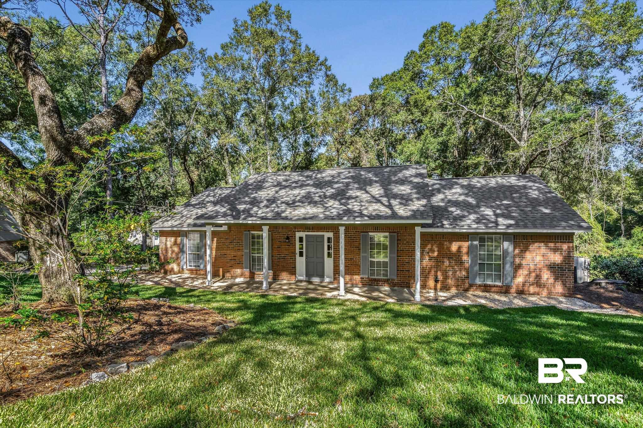 Single-story brick house with a covered porch, gray shutters, and mature trees around the lawn.