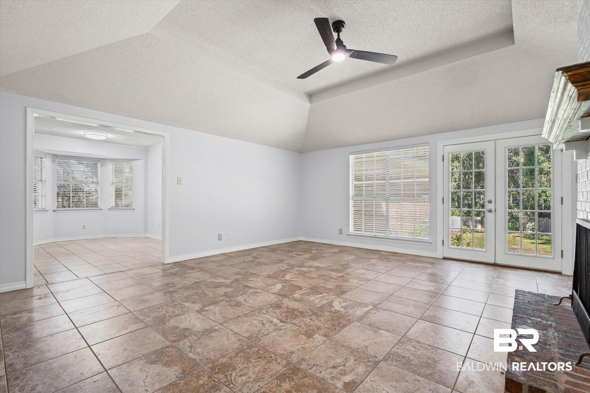 Vacant living room with tile floors, a ceiling fan, French doors, and a fireplace.