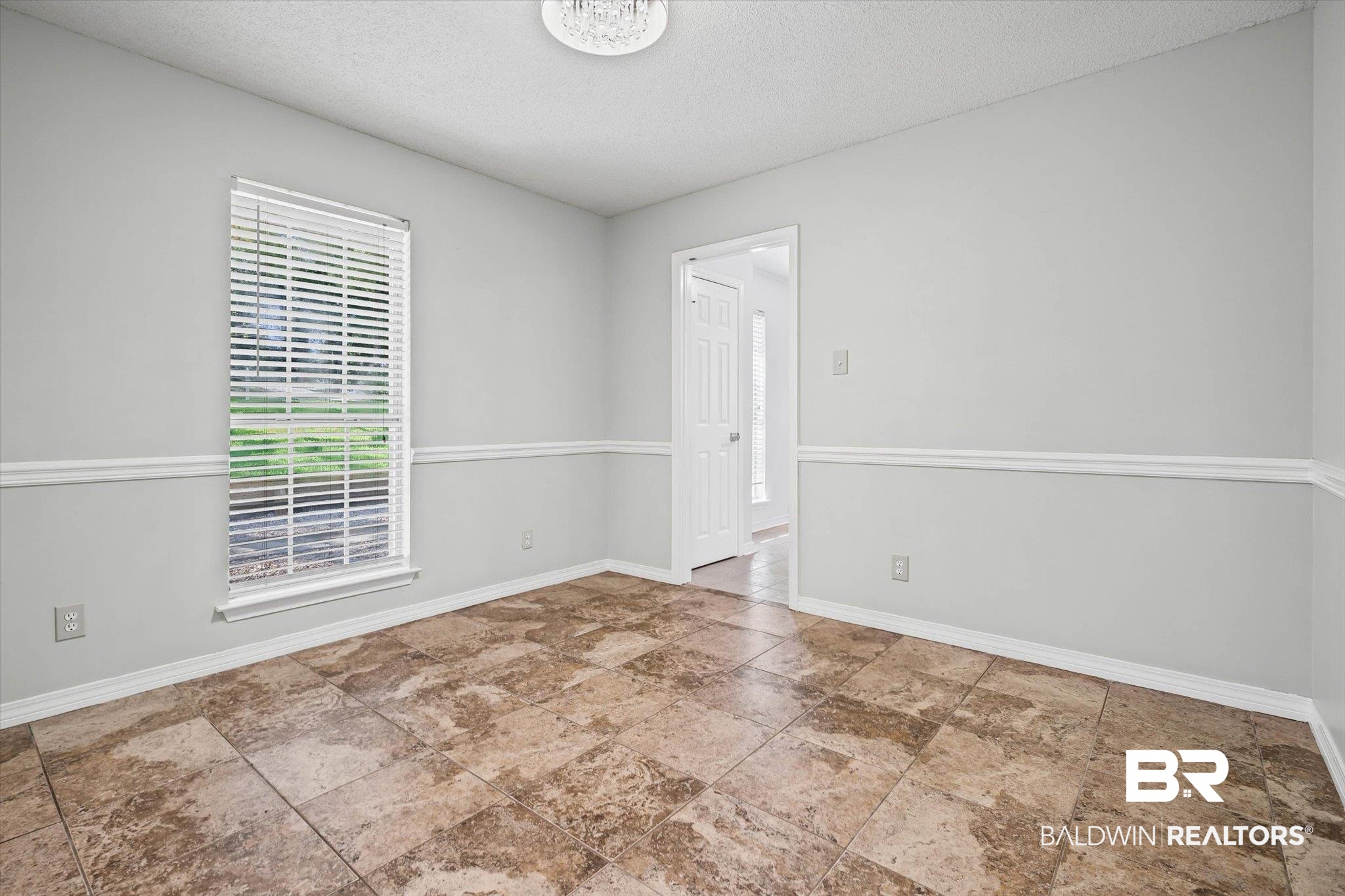 Empty room with brown patterned tile floors, gray walls, white chair rail, and a window with blinds.